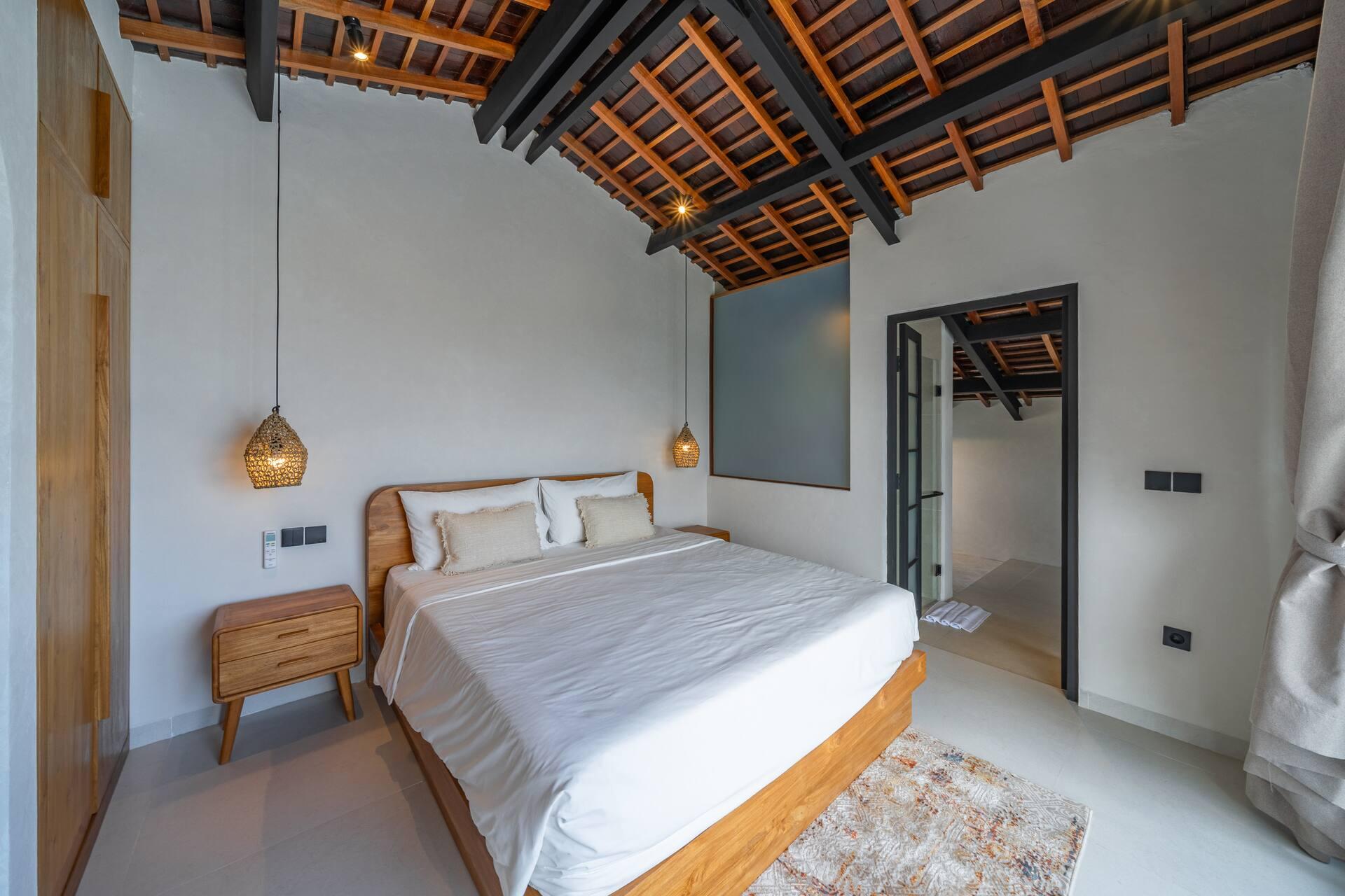 King bed under exposed timber rafters and terracotta roof tiles in the upper bedroom