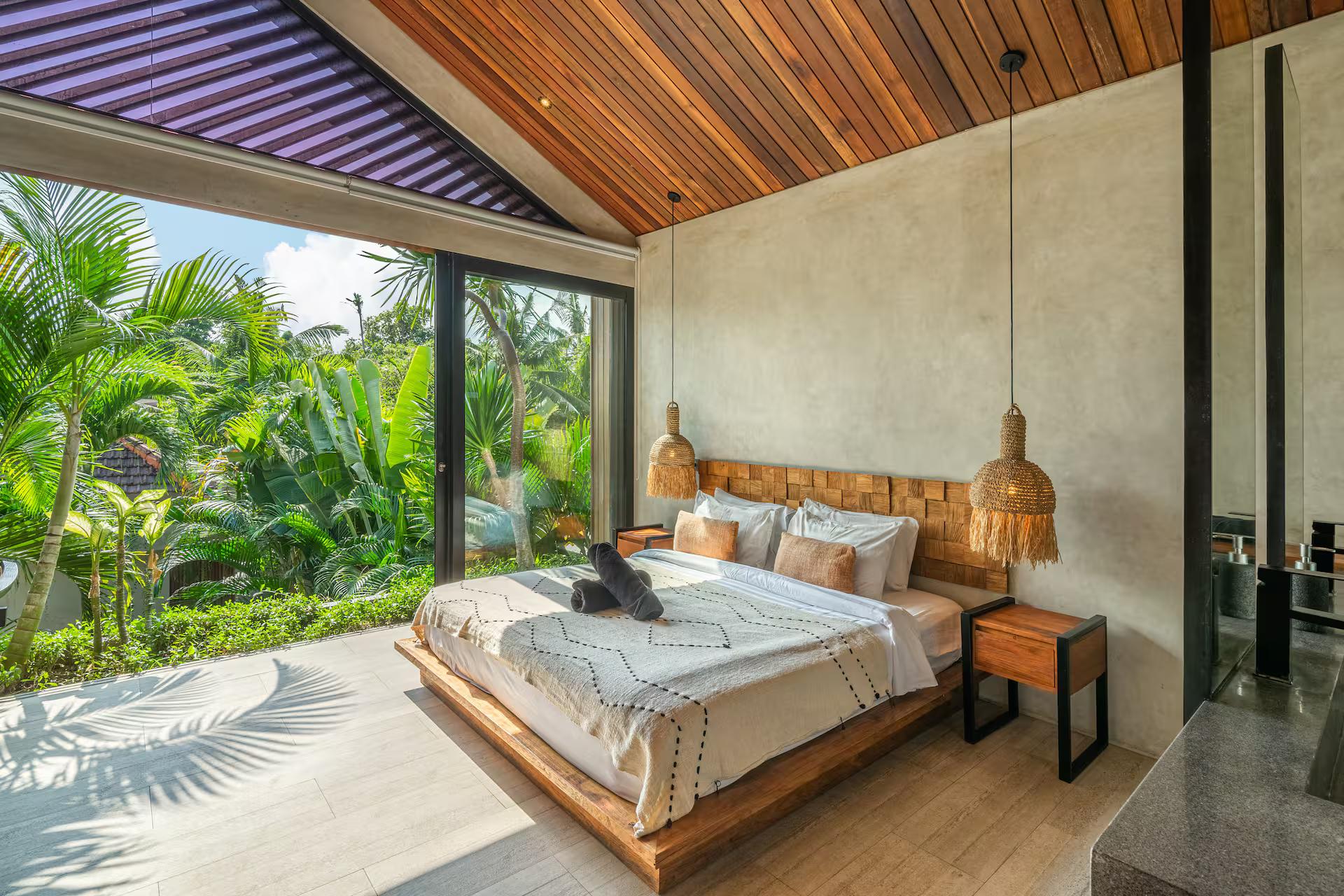 King bed low on a timber platform with glass on two sides looking into the palms