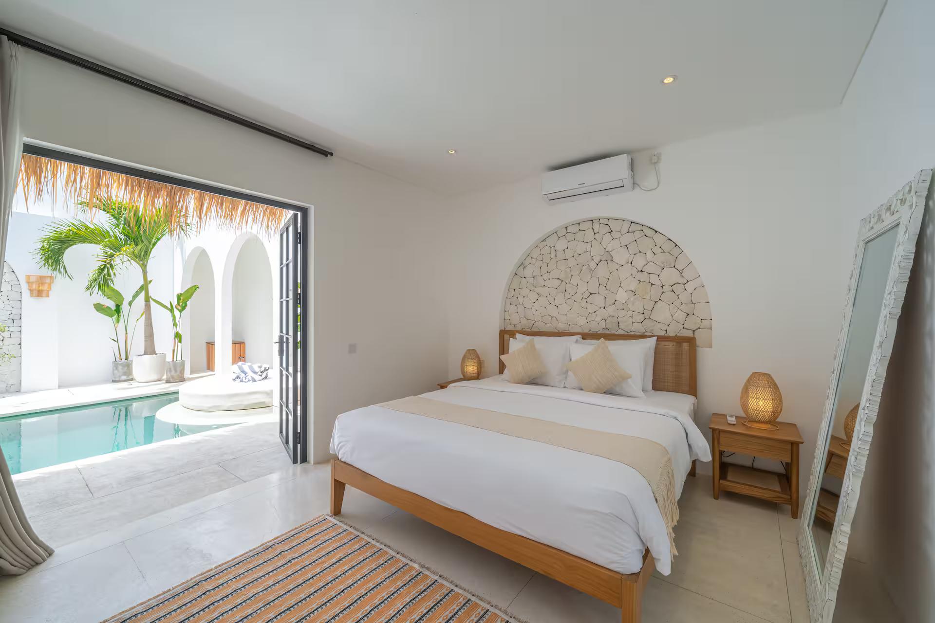 King bedroom at Villa Dusa opening to the pool terrace, river-stone arch behind the bed