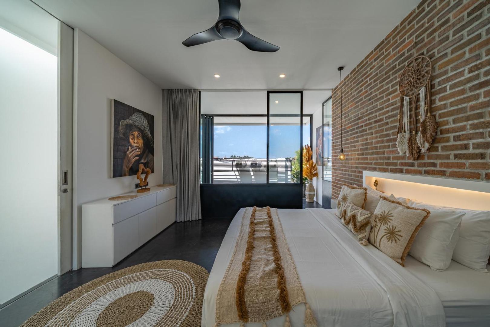King bed at Loft Erika against an exposed red-brick wall with a backlit floating headboard