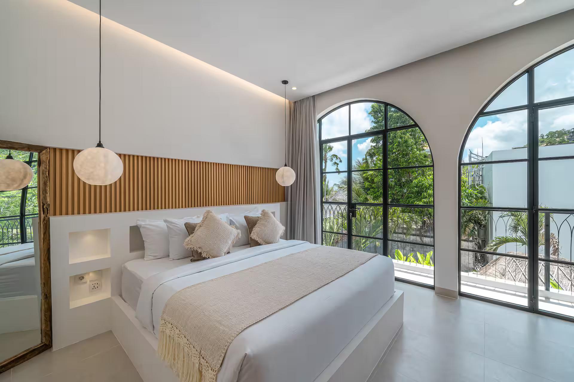 King bed beneath a fluted timber panel between two tall arched steel windows