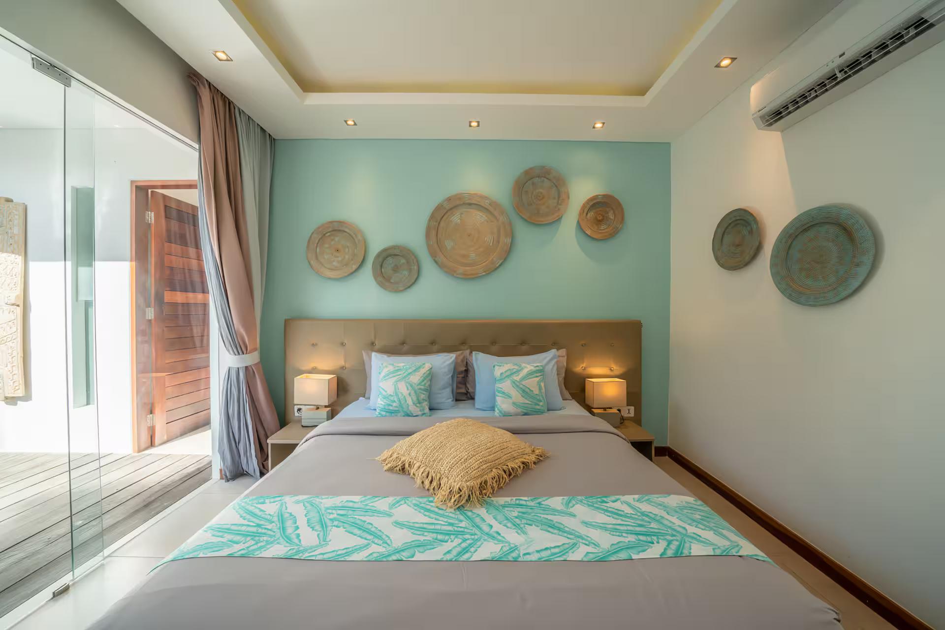 King bedroom with a mint-green wall hung with woven discs and doors to the pool