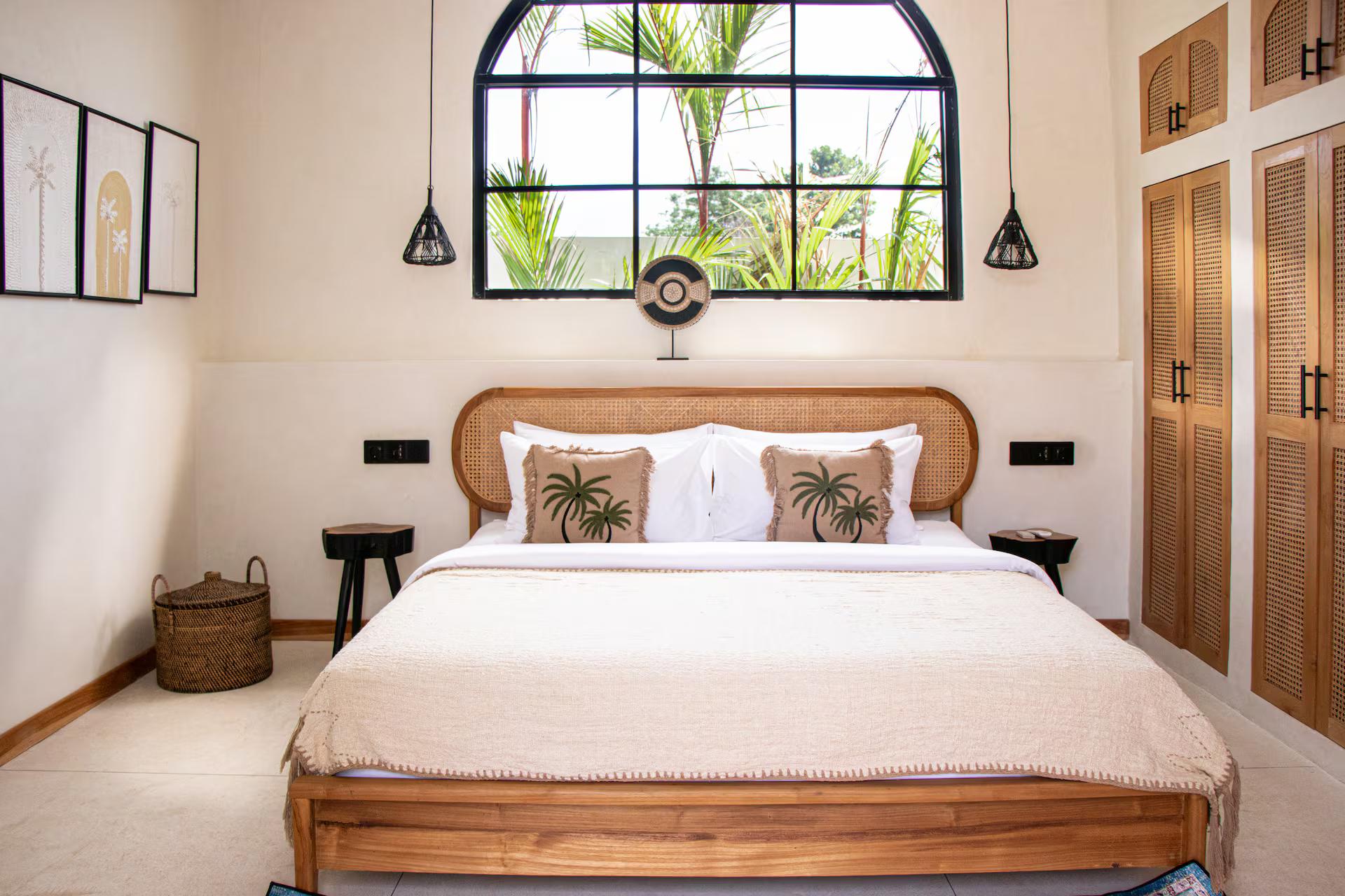 Bedroom with a curved cane headboard beneath a tall black-framed arched window