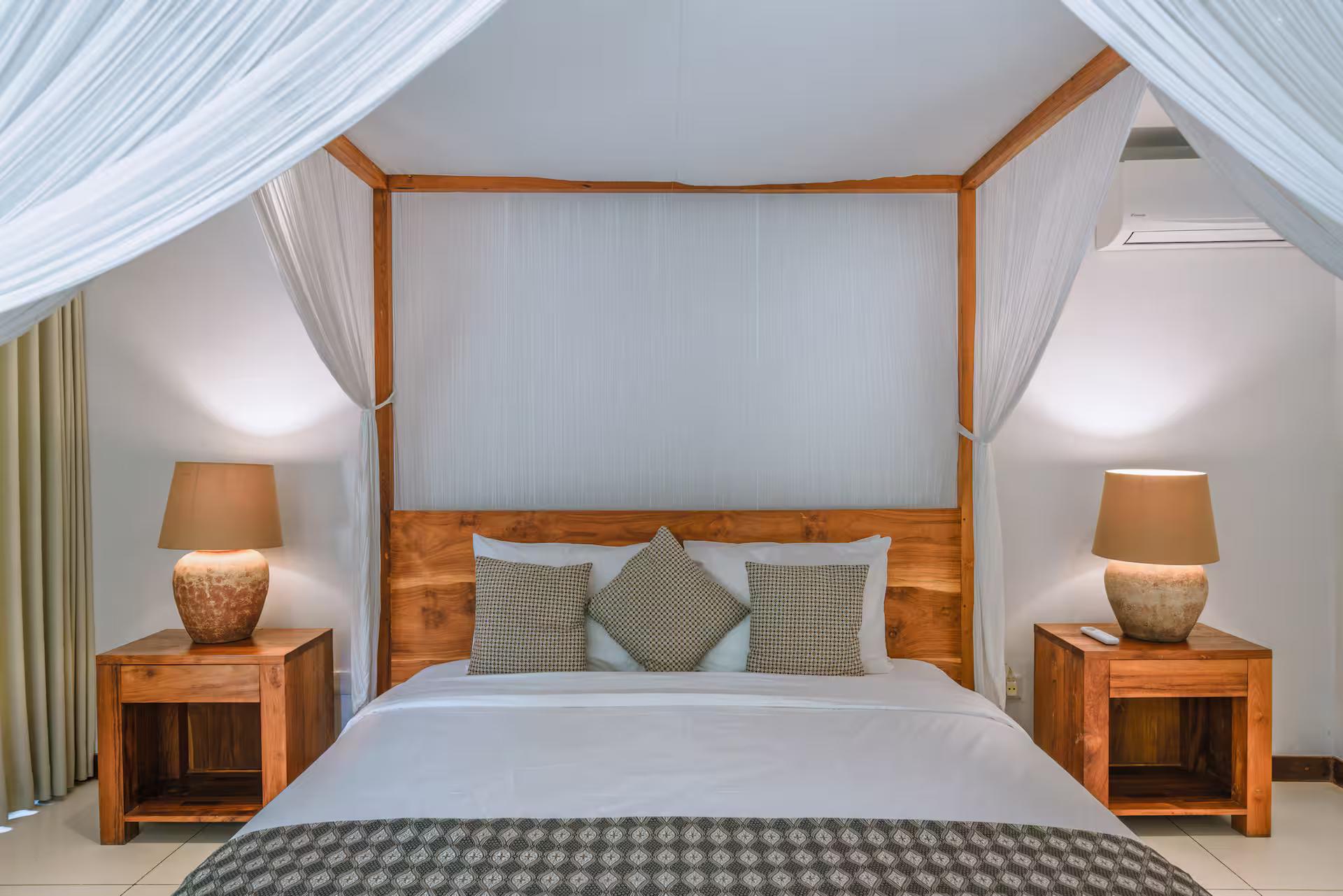 King four-poster bed draped in white mosquito netting under a high timber ceiling