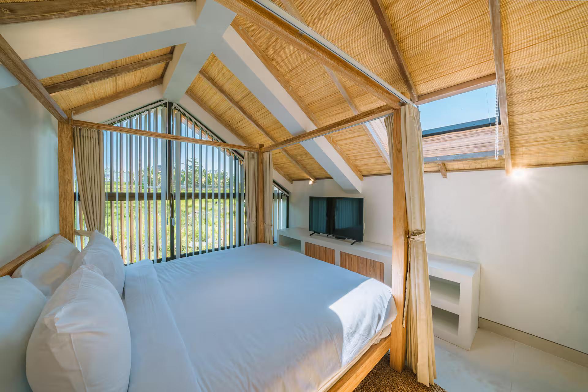 Four-poster bed on the mezzanine under a bamboo-lined gable, fields through the window