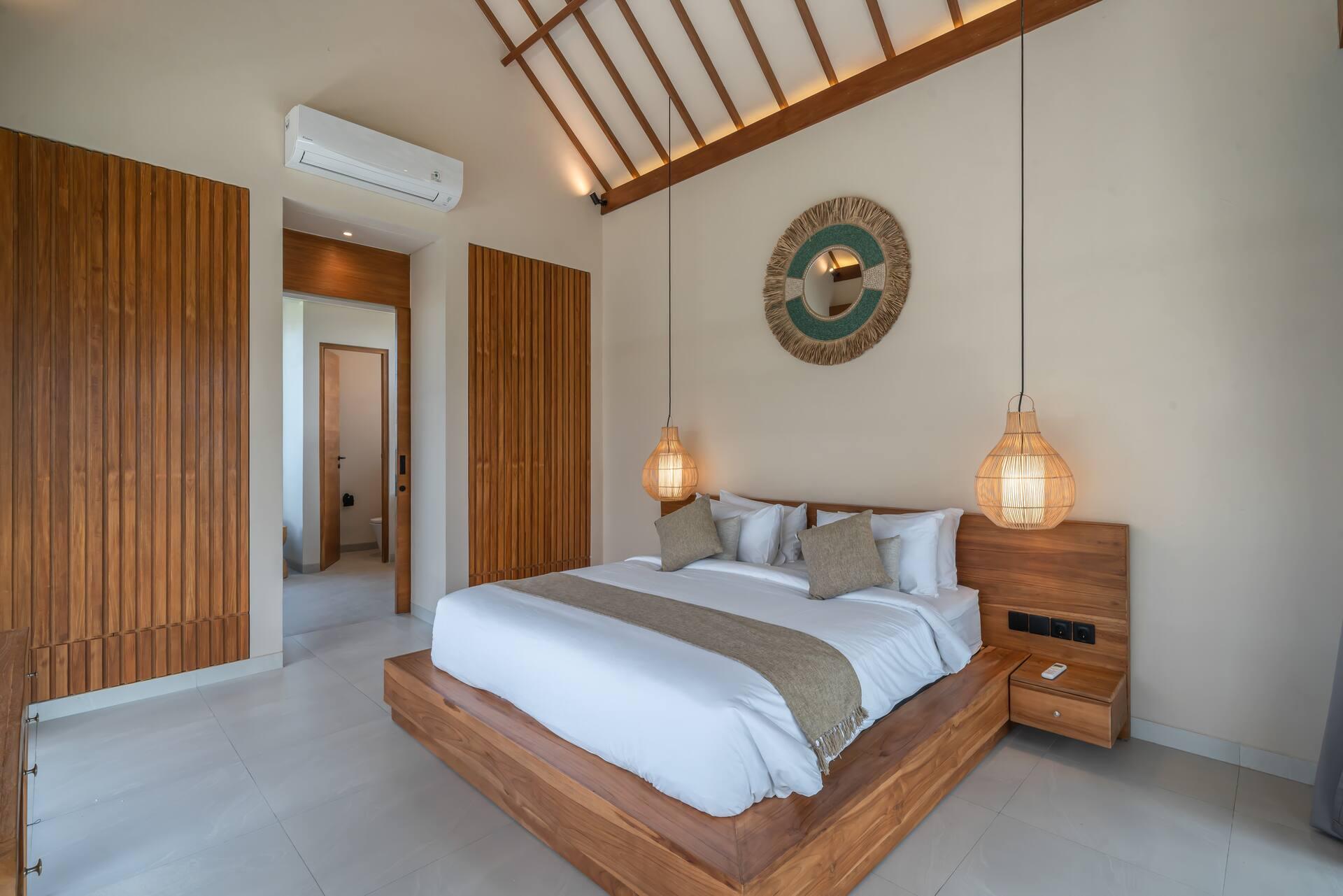 King bed against a teak-slatted wall with a carved Balinese medallion hung above it