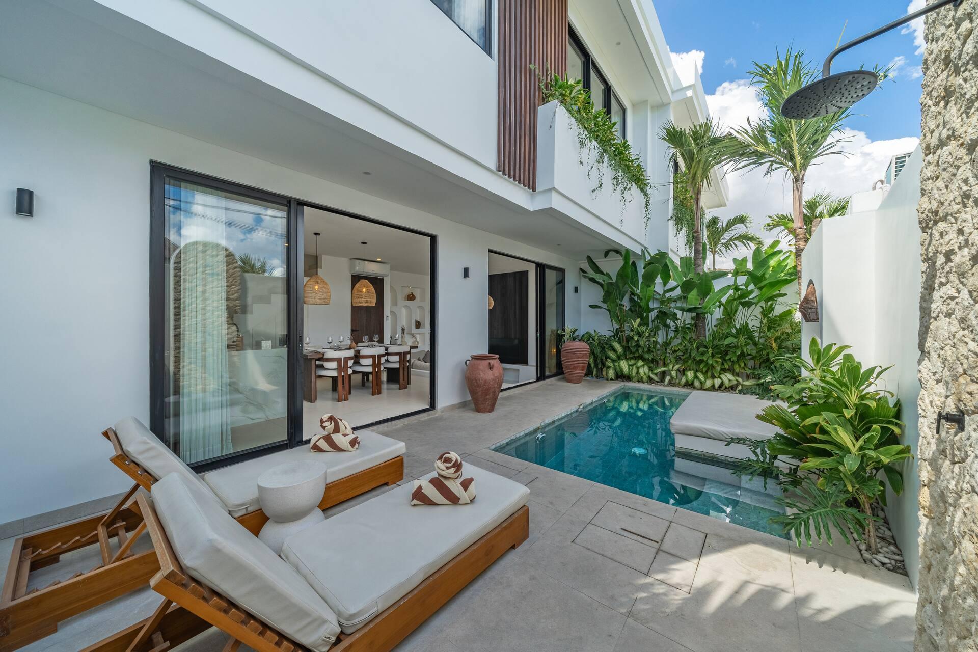 Twin timber sun loungers on the pool terrace, with the villa's folding glass doors open to the dining room behind