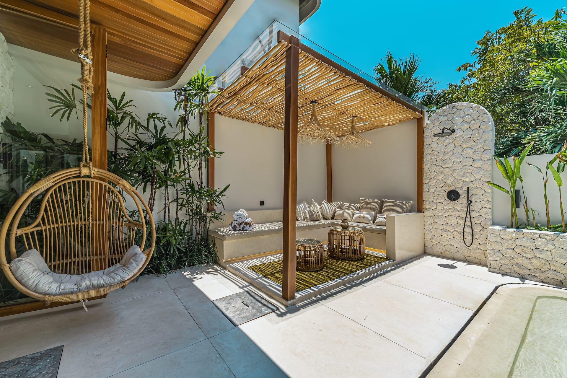 A rattan hanging chair swings beside the outdoor lounge and the arched stone rain shower
