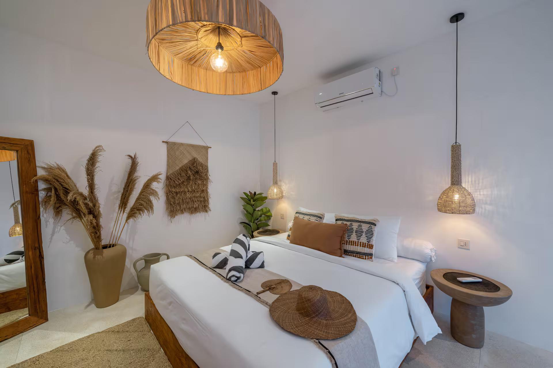 King bedroom with woven wall hangings, a pendant either side and a leaning floor mirror
