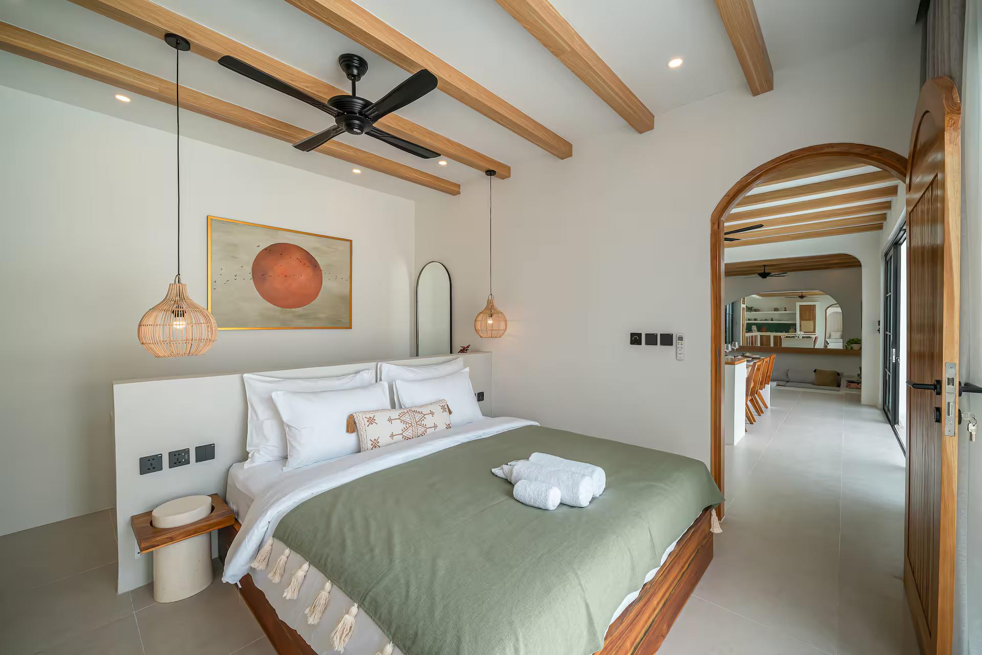 Queen bedroom with an olive bedspread, rattan pendants and an arched door to the en-suite