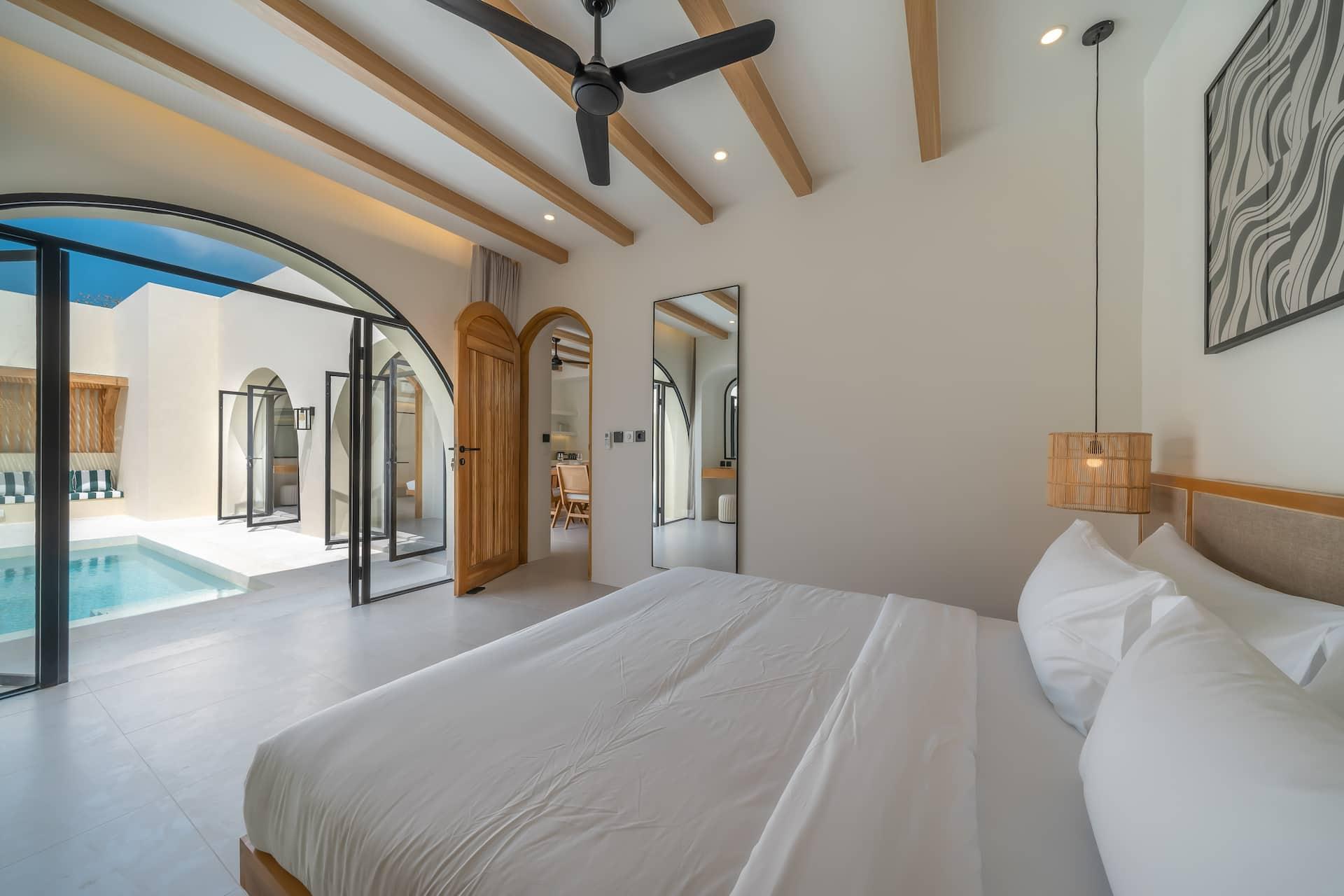 Master bedroom with arched doors folded back to the pool, the bed on a solid timber base
