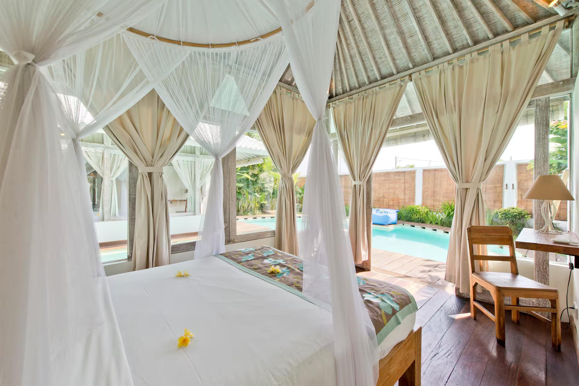 Four-poster bed under a white mosquito net looking straight out to the pool