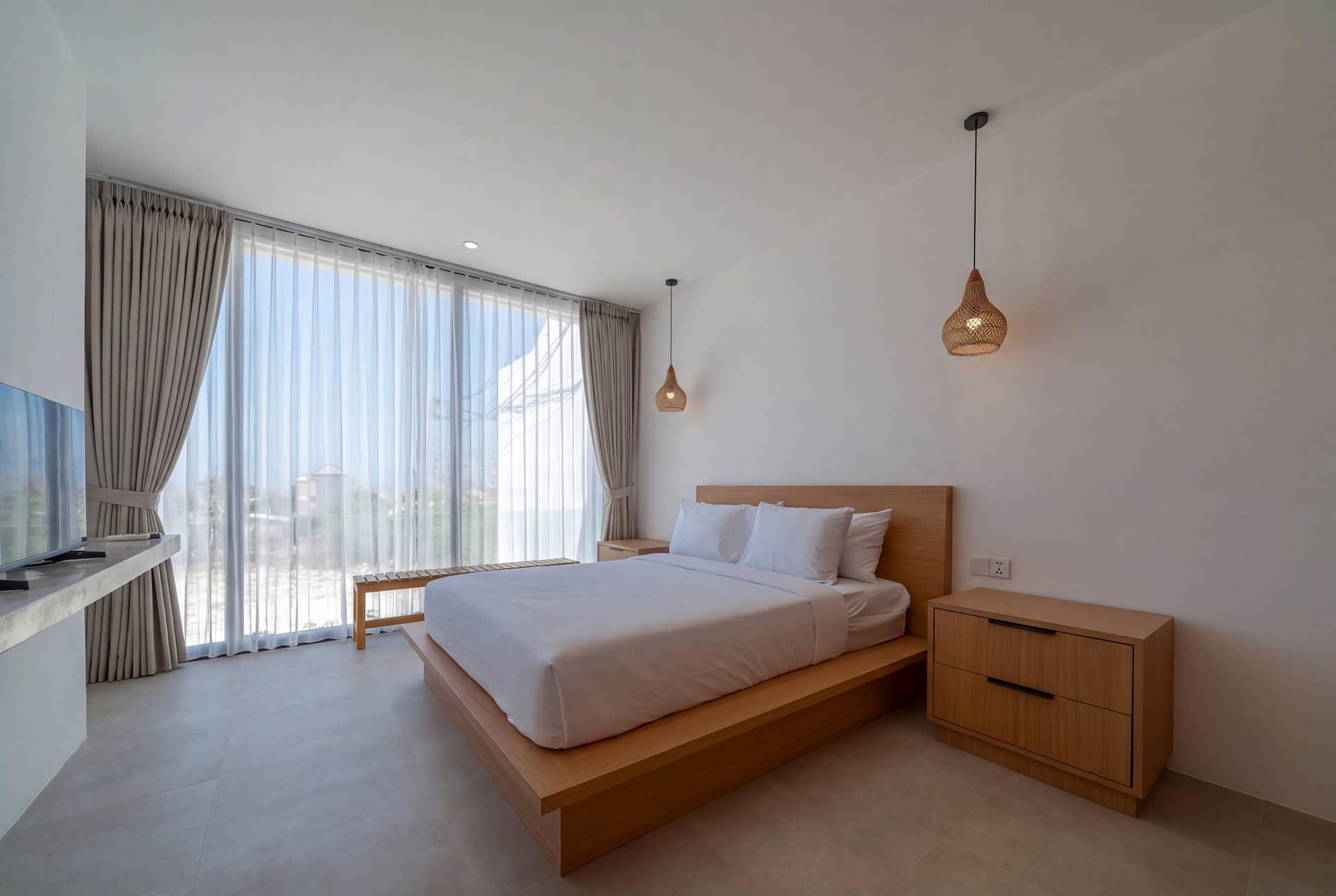 Villa Merine bedroom with a bed on a low timber base and sheer curtains over floor-to-ceiling windows