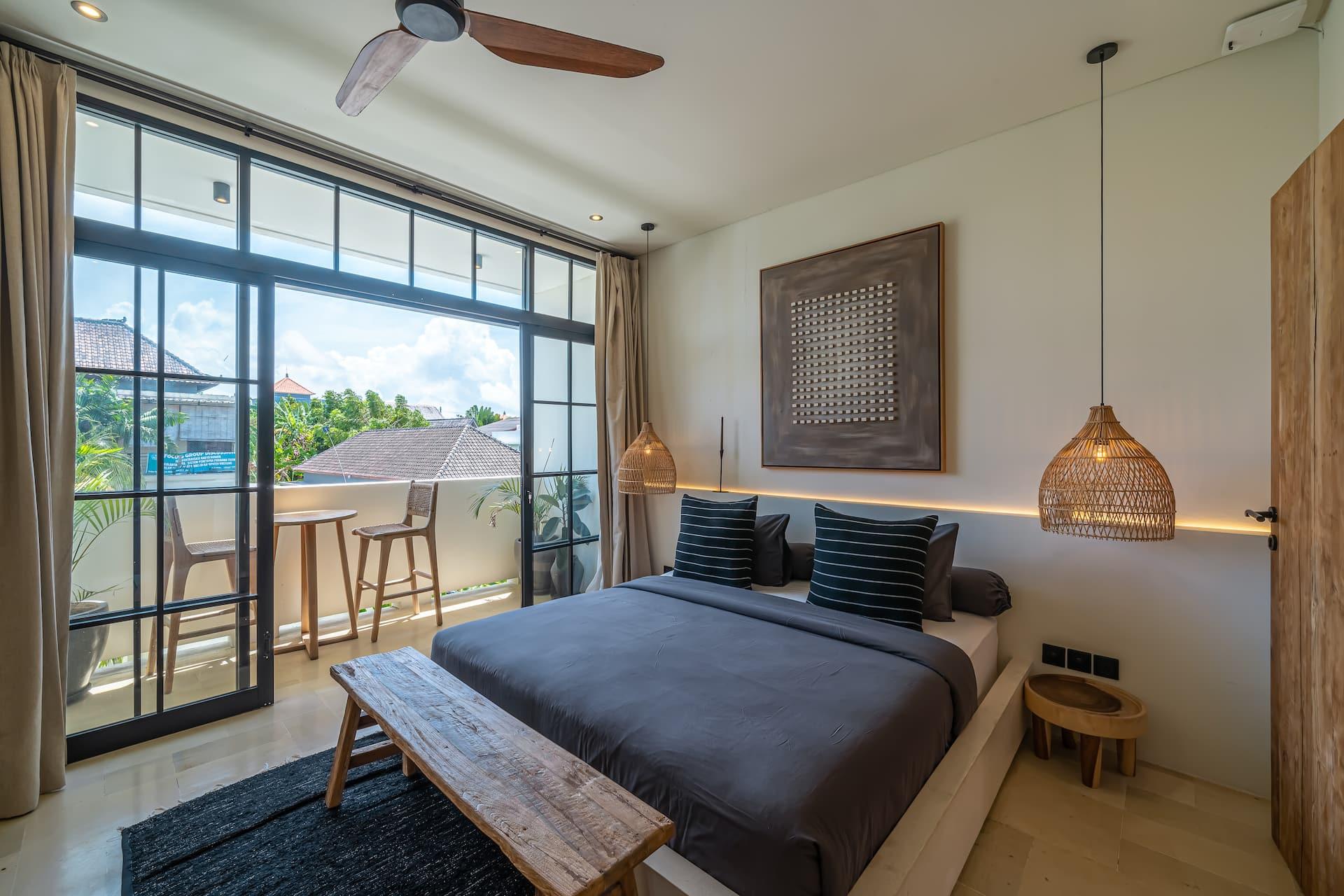 Villa Ania's upstairs bedroom with a reclaimed timber bench, rattan pendants and glass doors to a private balcony