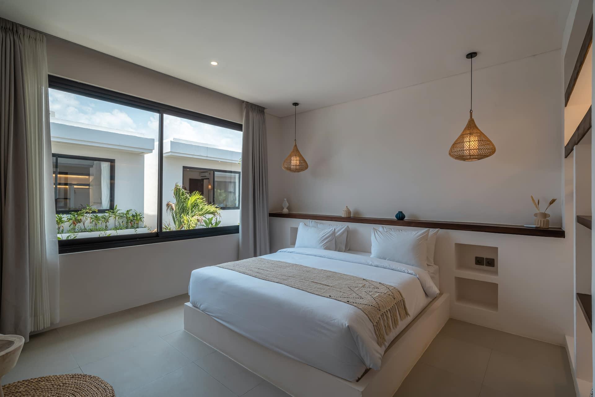 Villa Nyra upstairs bedroom with a large white bed, a floating timber shelf and a wide black-framed window