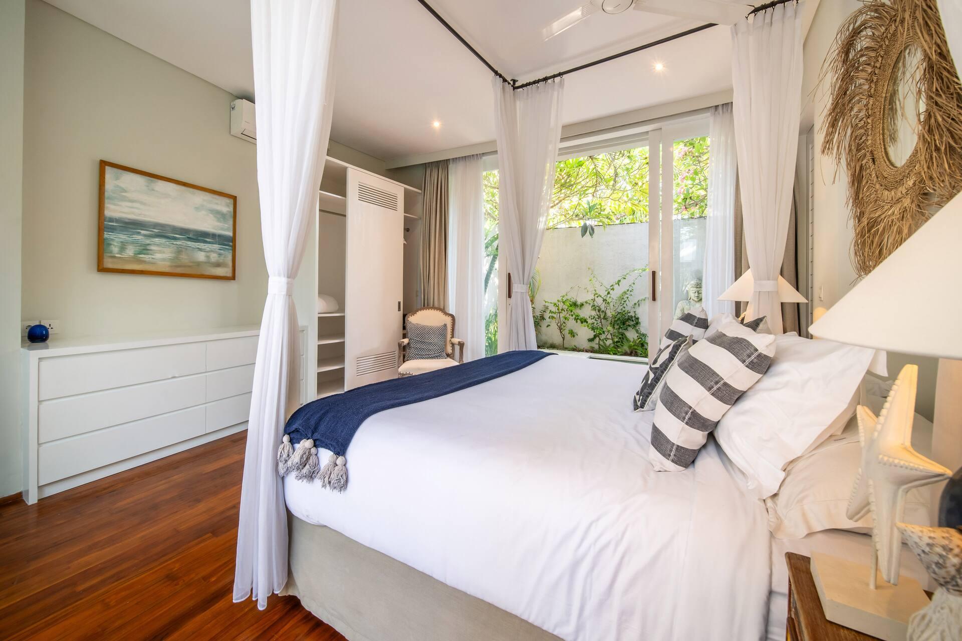 Master bedroom with a four-poster canopy bed, striped cushions and doors to the garden