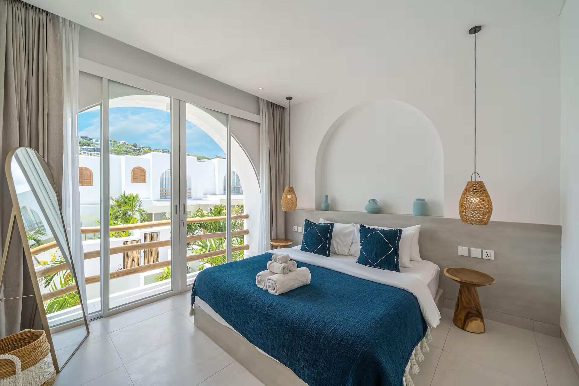 King bedroom in teal and off-white, sliding doors open to the timber-railed balcony