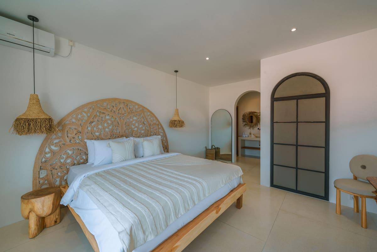 Bedroom with a round carved timber headboard and an arched black steel door to the garden