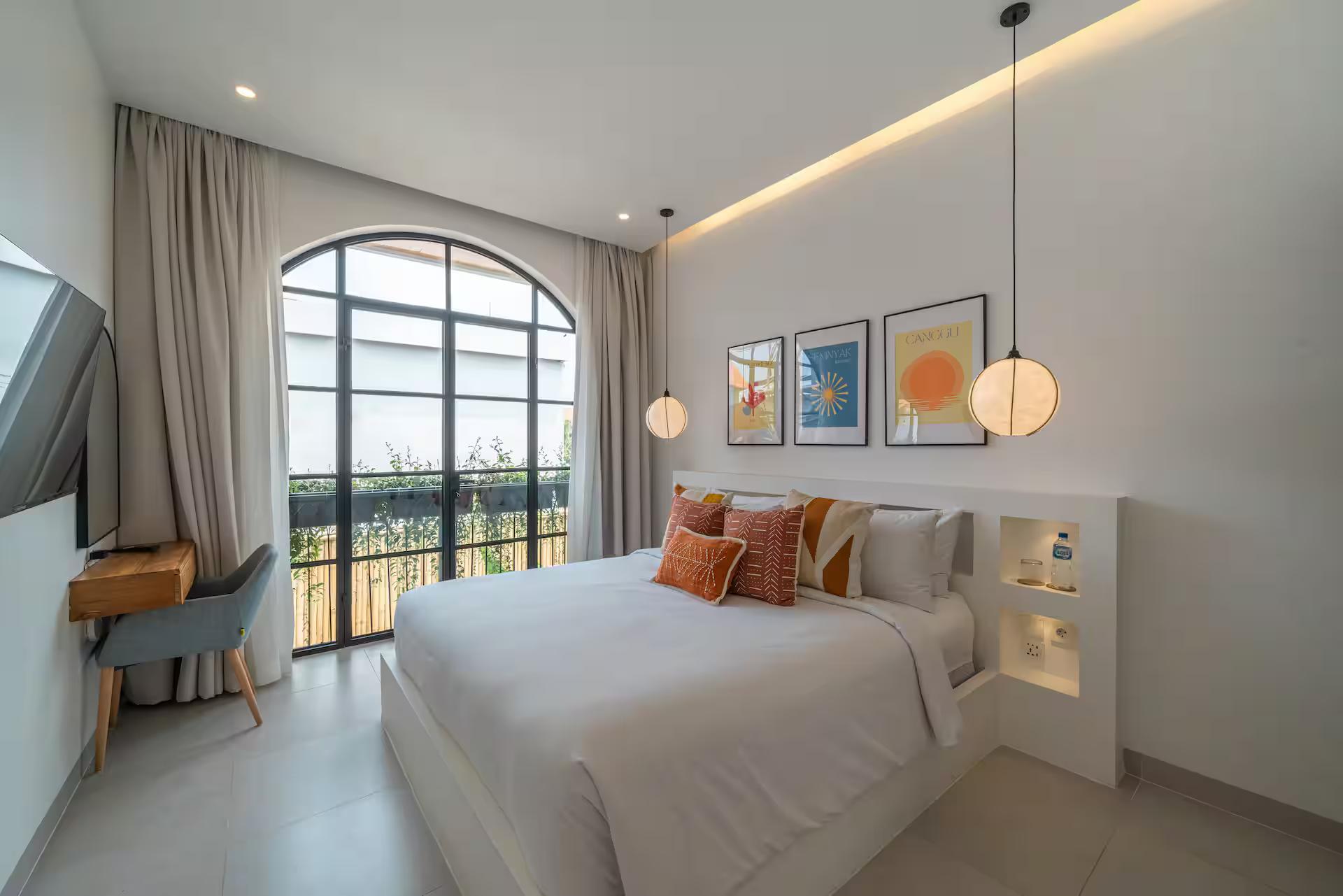 King bedroom with an arched window onto a Juliet balcony, a desk and framed prints