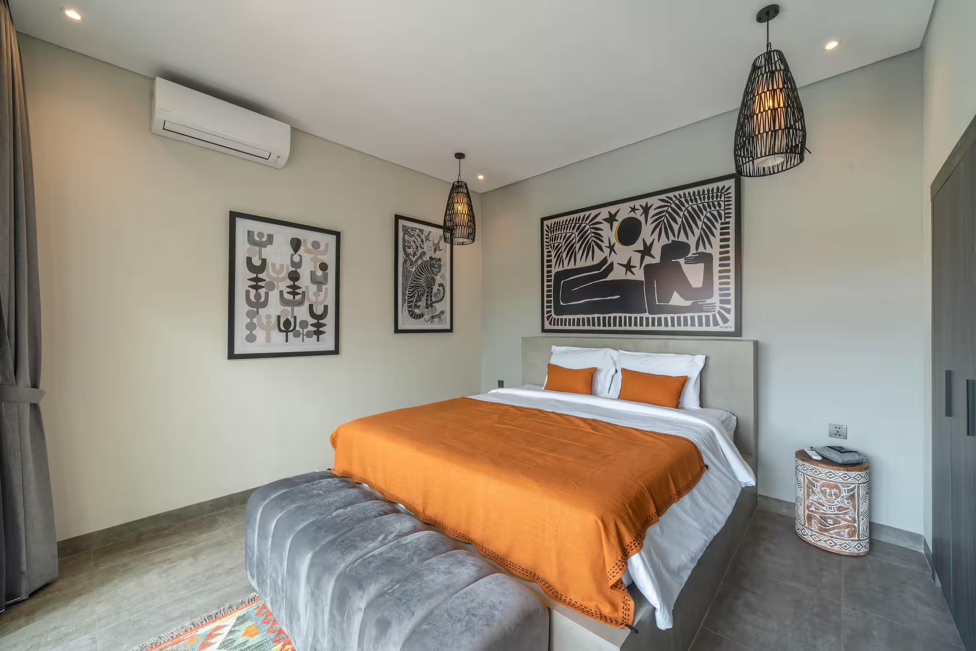 King bedroom with a burnt-orange throw and framed line drawings above the bed