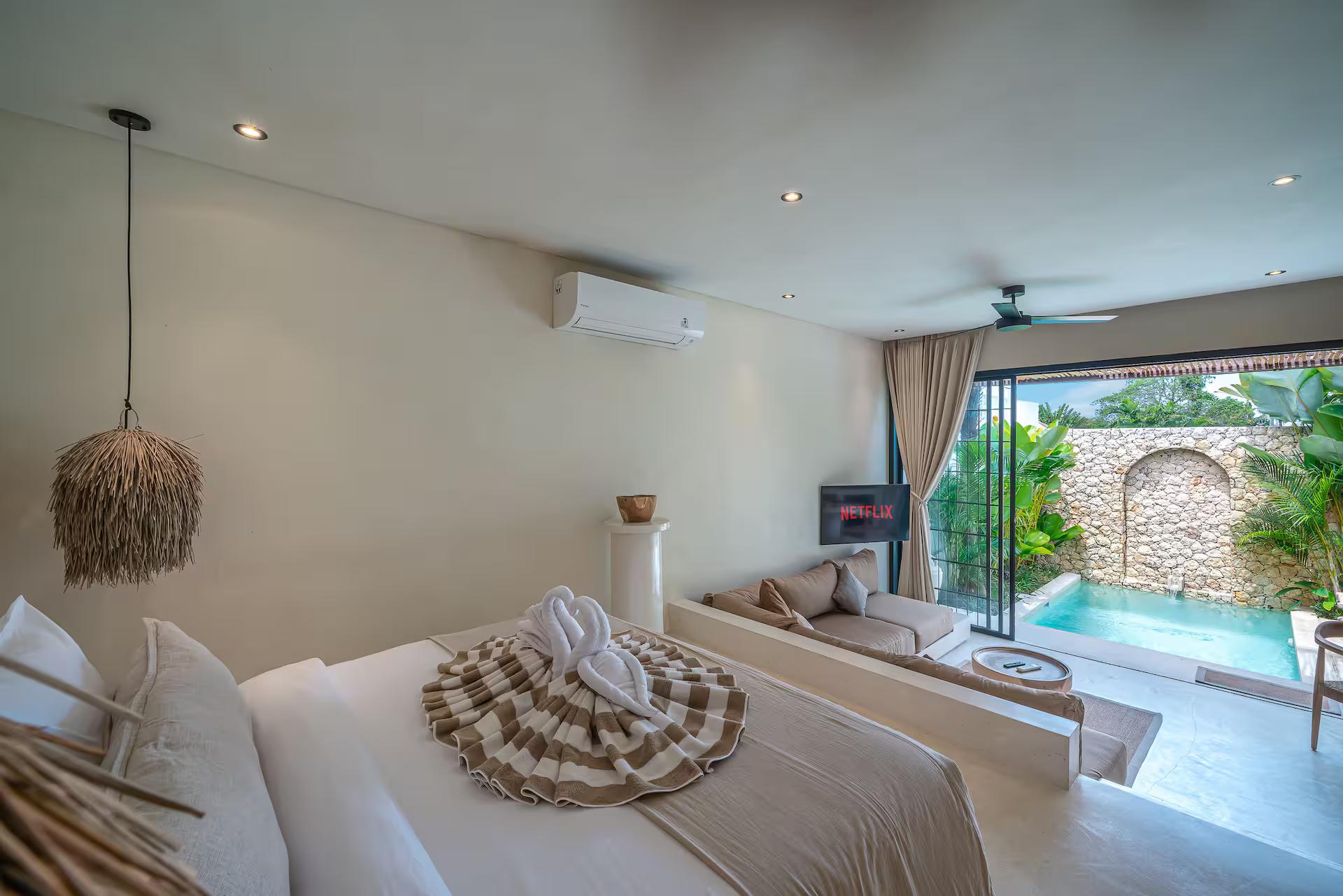 Queen bed with a woven throw, looking out through black-framed glass to the pool