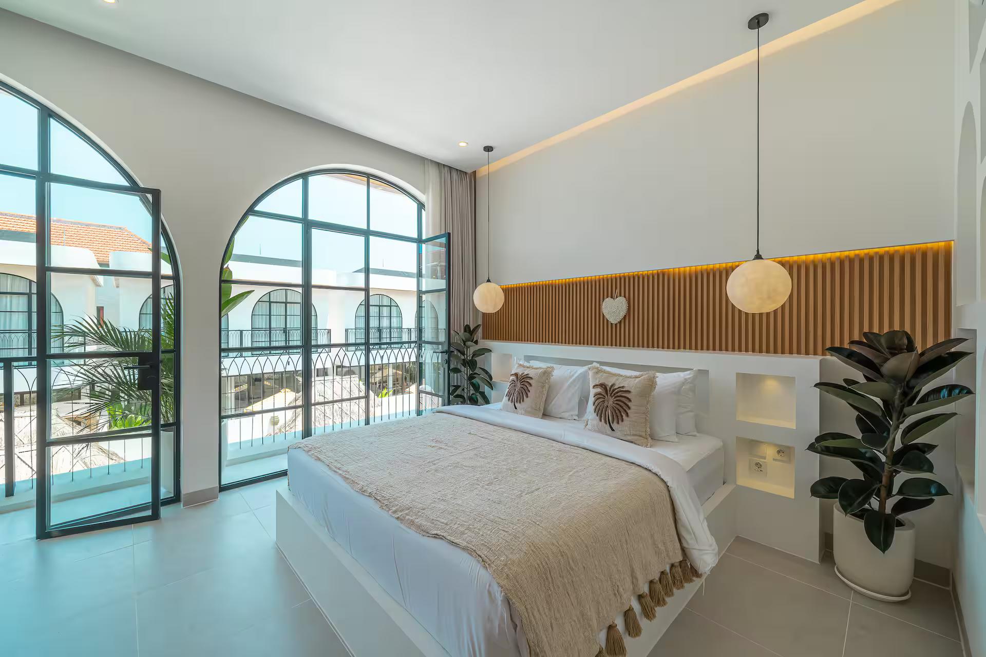 Bedroom at Villa Arnie with a fluted timber headboard and arched steel doors to the balcony