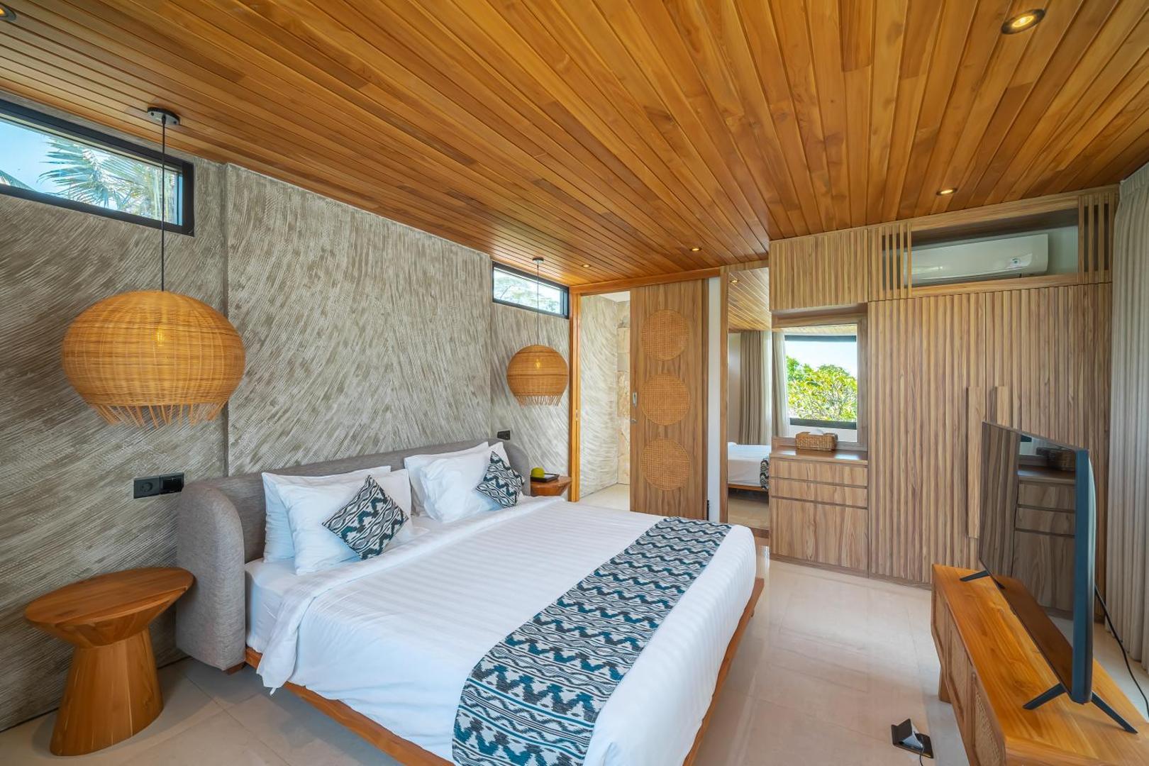 Master bedroom at Villa Arunika under a timber-battened ceiling, rattan pendant beside the bed