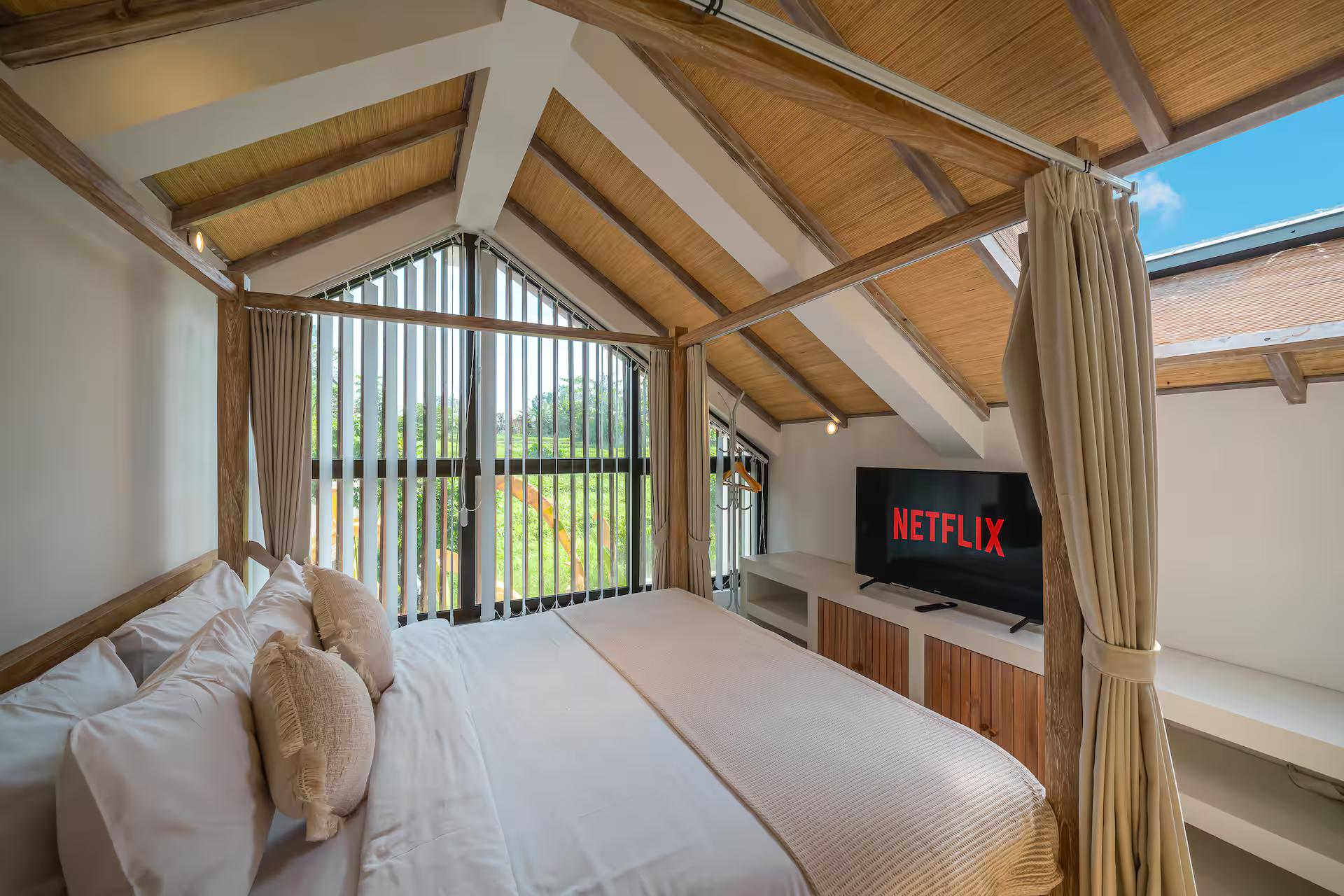 Sleeping loft at Villa Tiny 2 under exposed rafters, gable window and a smart TV