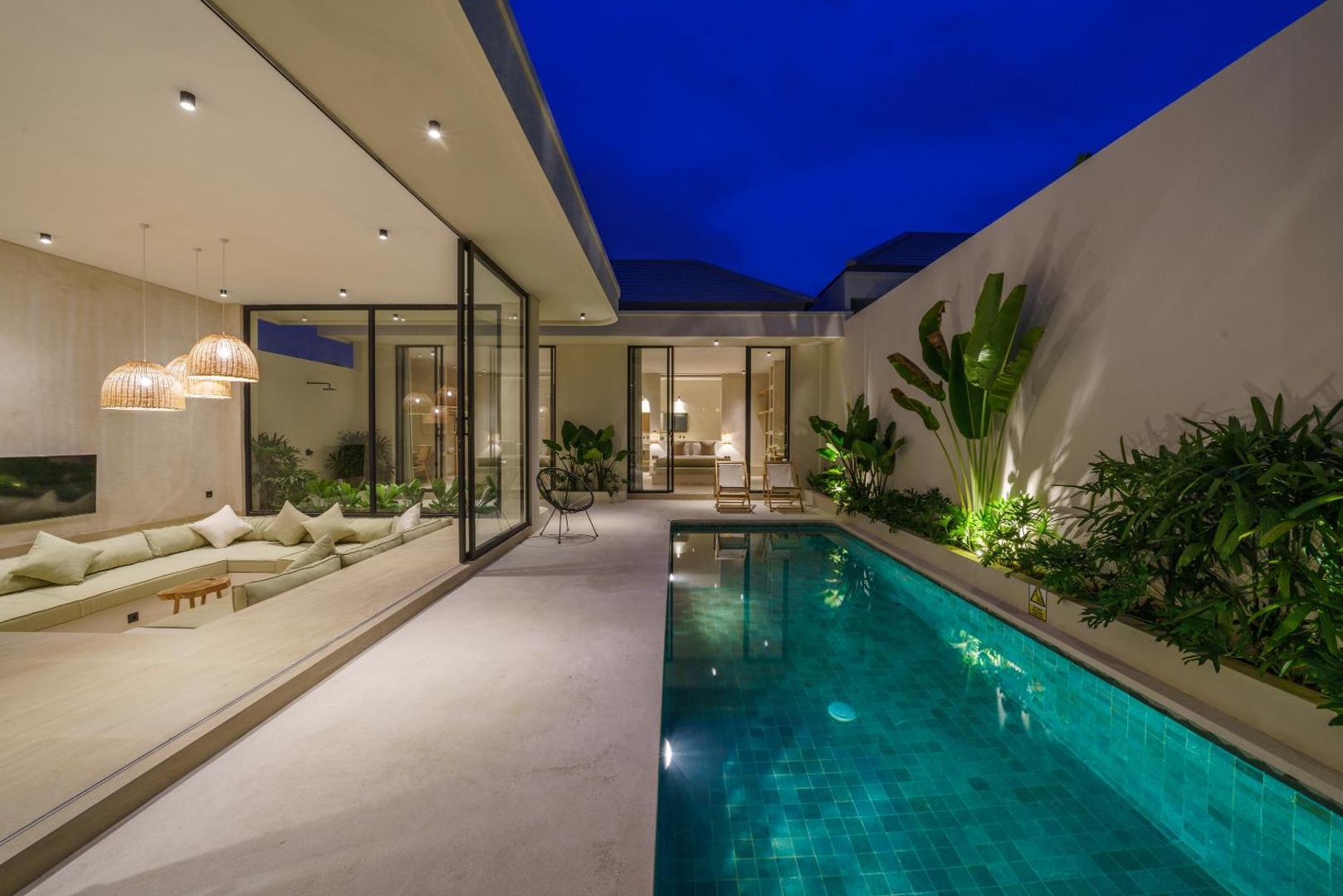 The pool lit deep green at dusk, seen from the sunken lounge through open glass walls