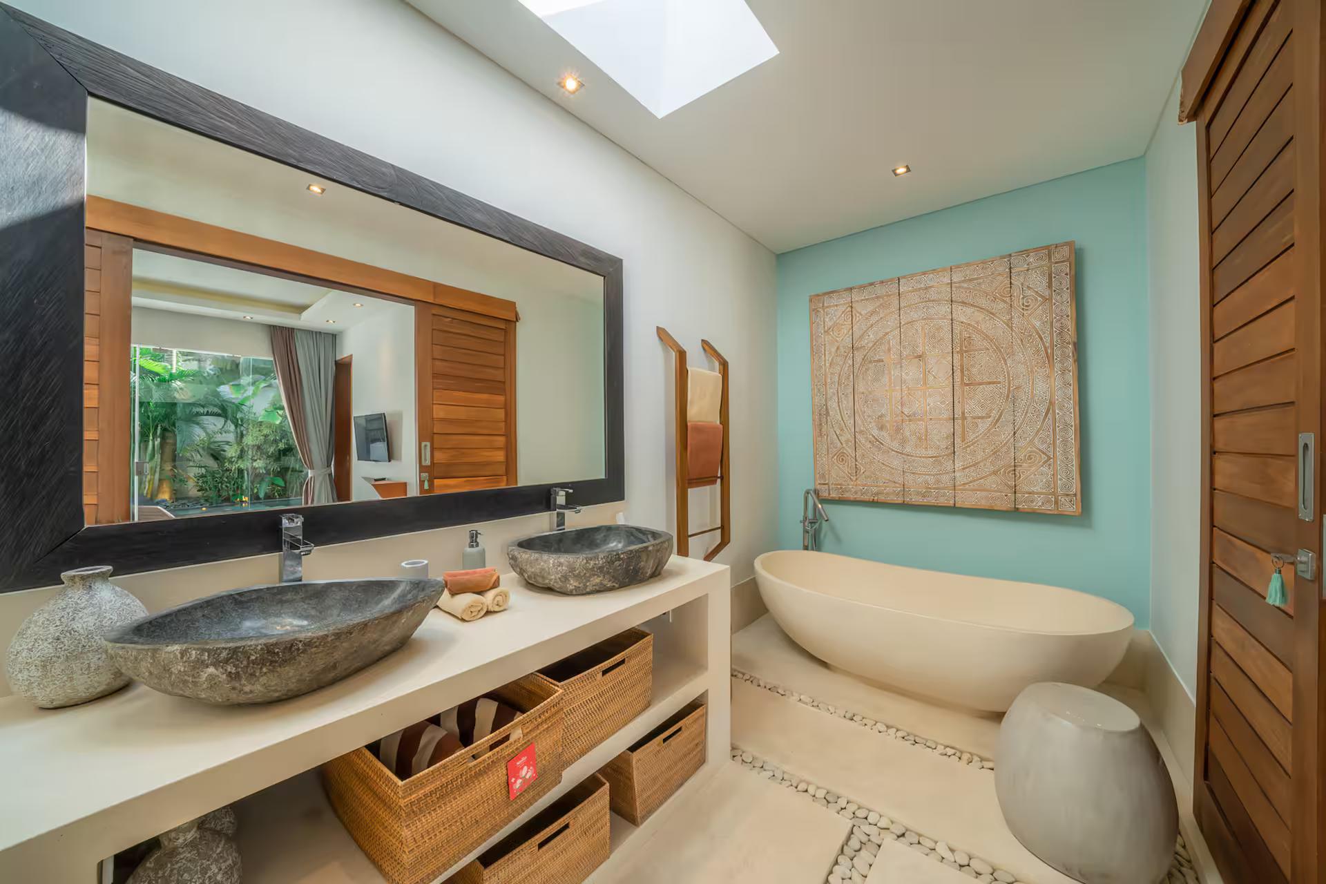 Freestanding oval tub under a skylight beside twin river-stone basins at Villa Cuatro