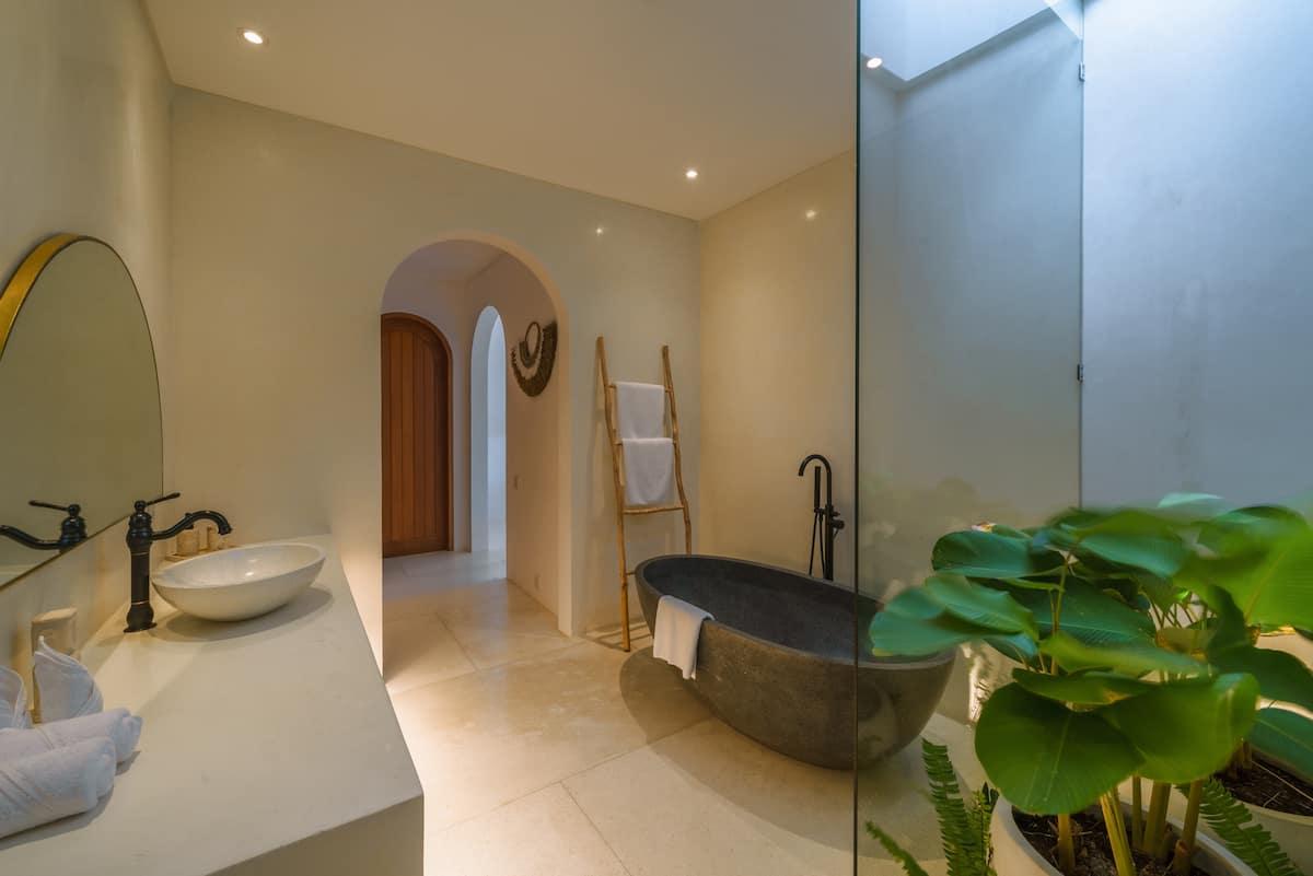 A volcanic-stone bath at Villa Eliad set beside a glazed light-well of elephant-ear plants