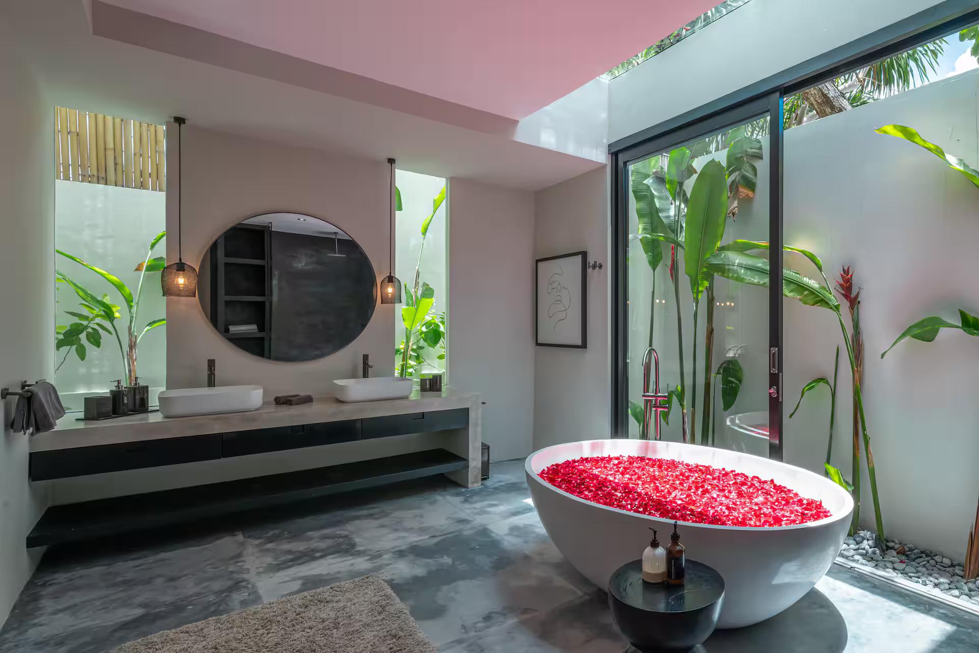 Oval tub filled with red petals beneath twin round mirrors, banana palms in the courtyard