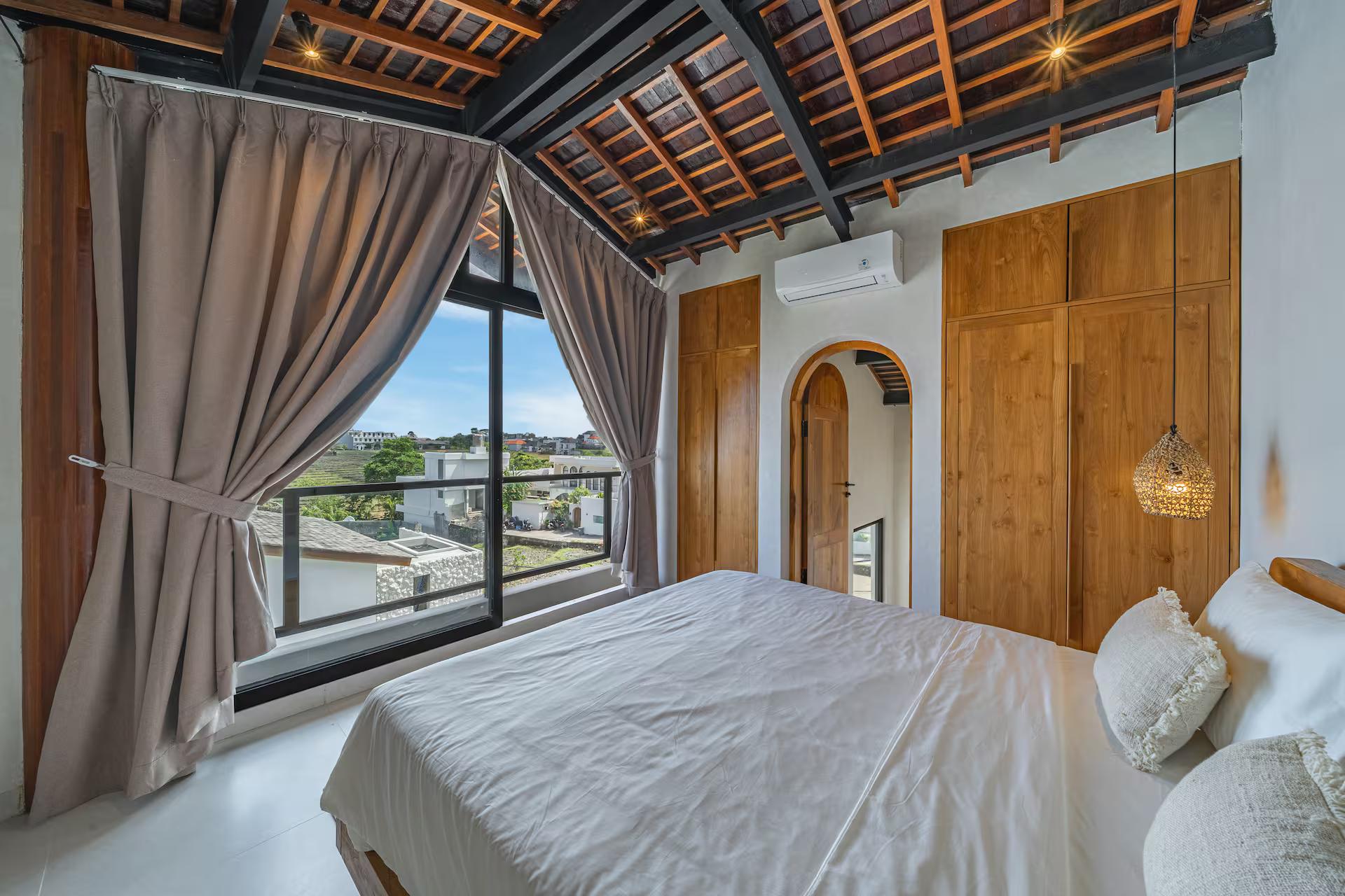 Picture window over village rooftops beside the king bed in the top-floor bedroom at Villa Terra Calma