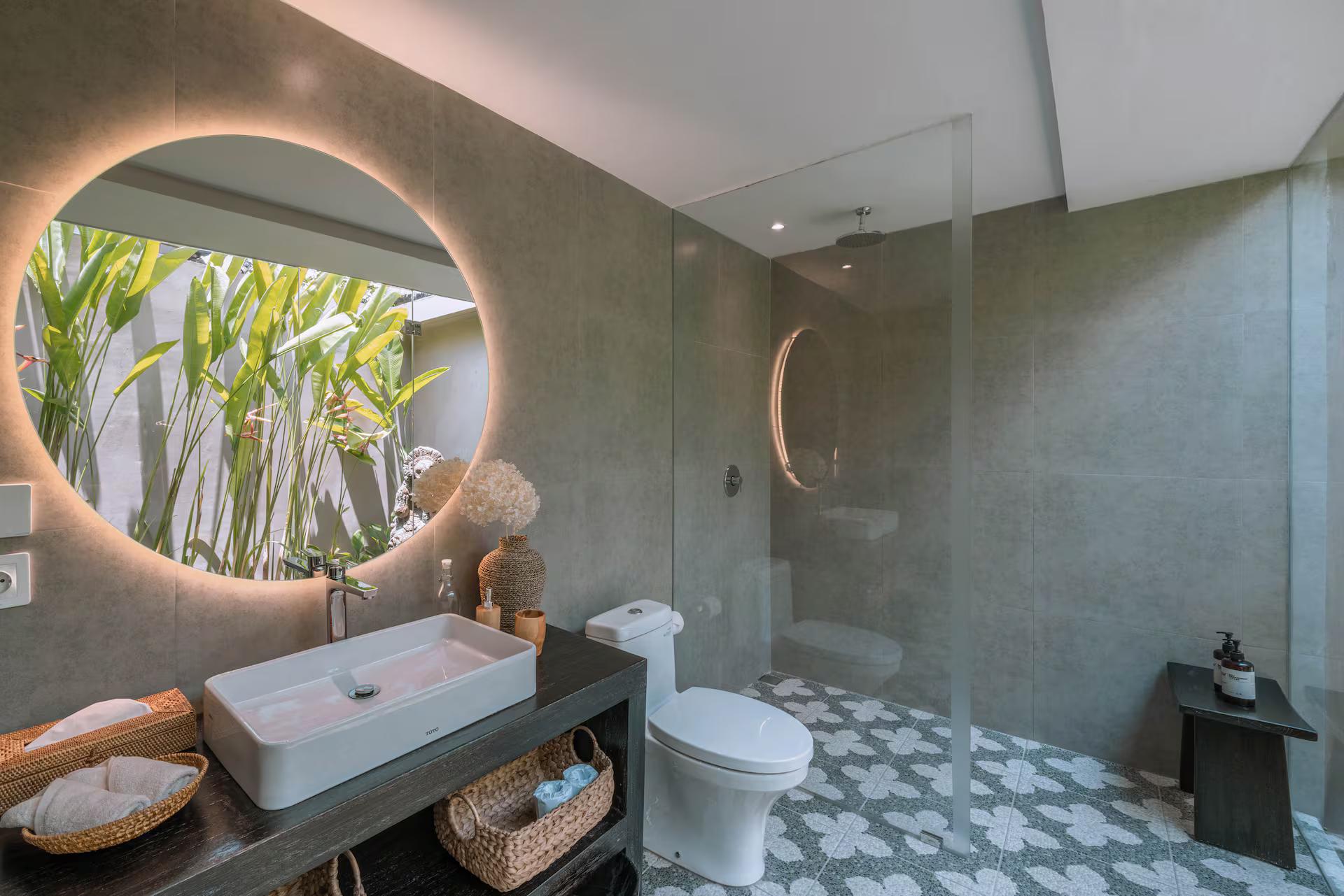 En-suite in polished grey cement with a round backlit mirror and a stone vessel basin