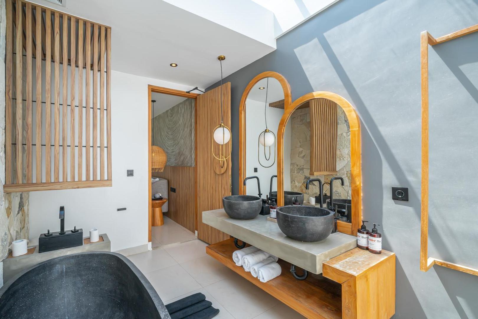 Black river-stone oval bath and twin stone basins under arched timber mirrors