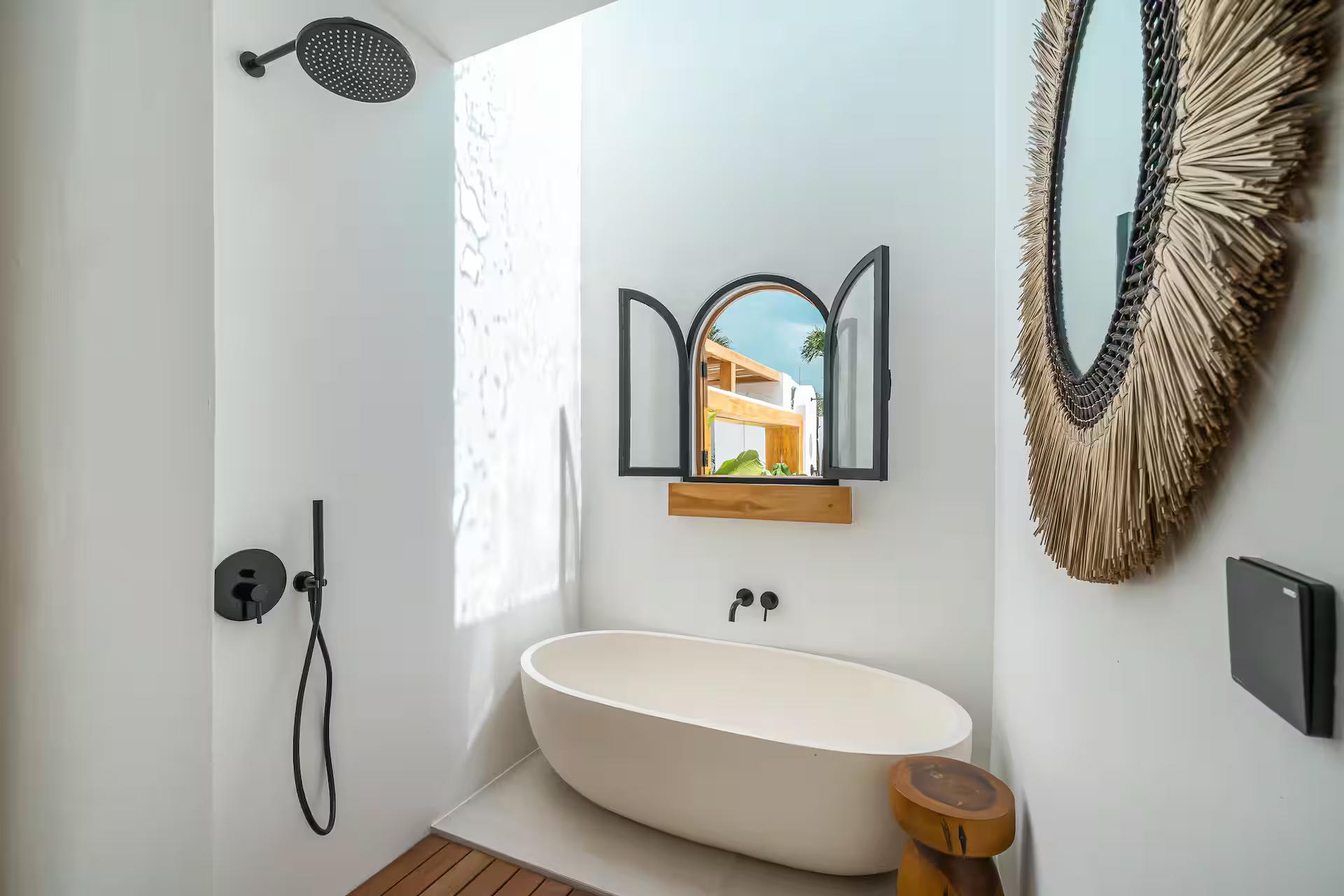 Freestanding oval tub beneath a rattan sunburst mirror, black rain shower alongside