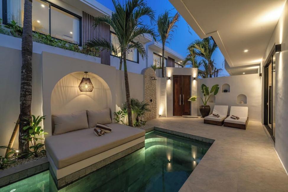 Nova Oasis 4 after dark, the pool lit green beside the daybed and timber loungers