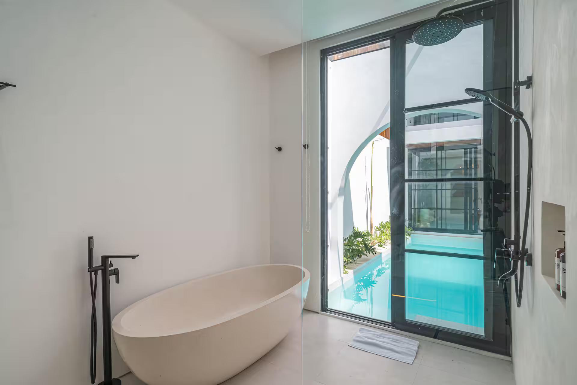 Freestanding oval tub set beside glass doors that open straight onto the pool