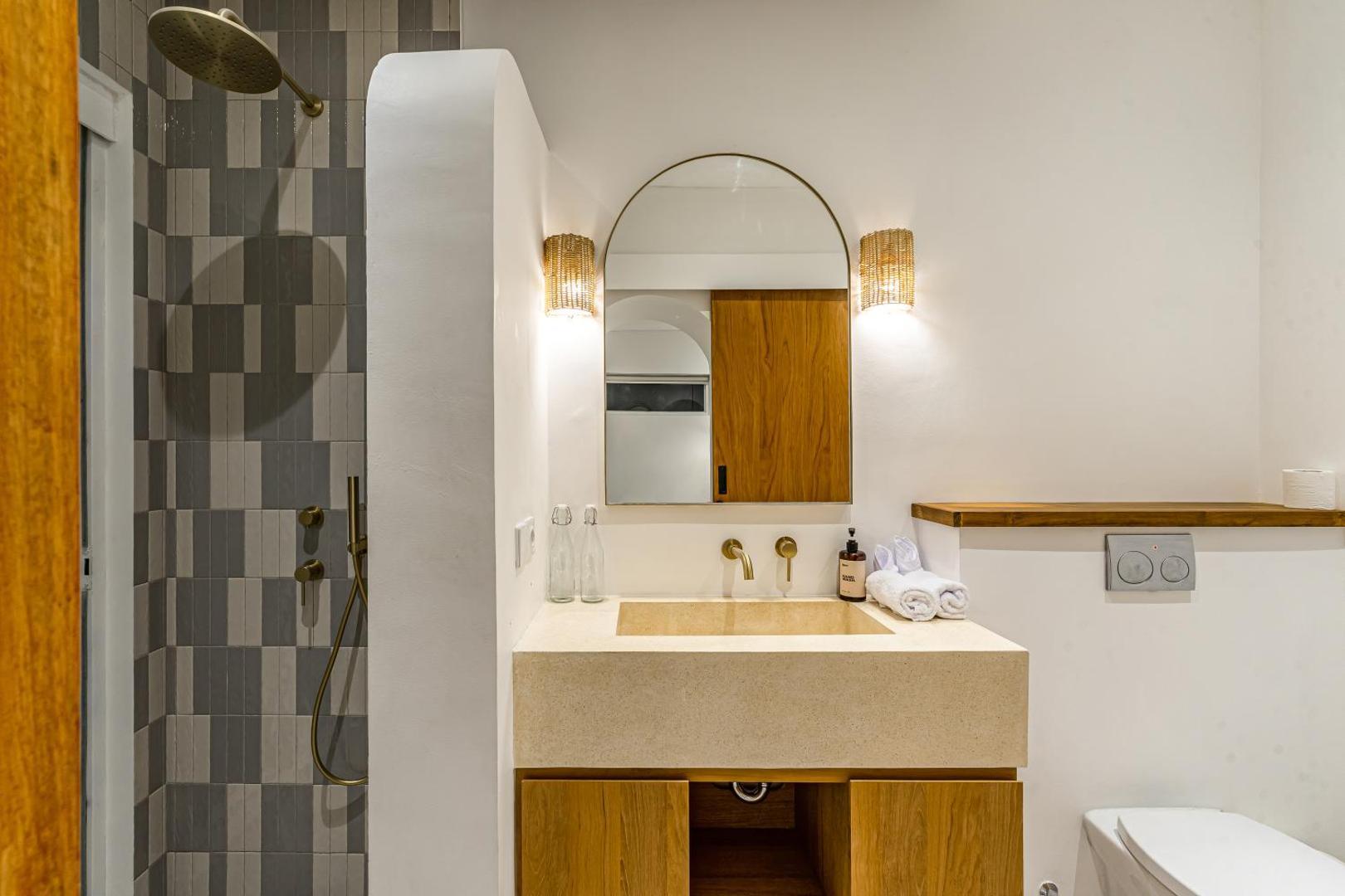 Bathroom lined in stacked grey-green tile, with a stone trough basin and brass tapware