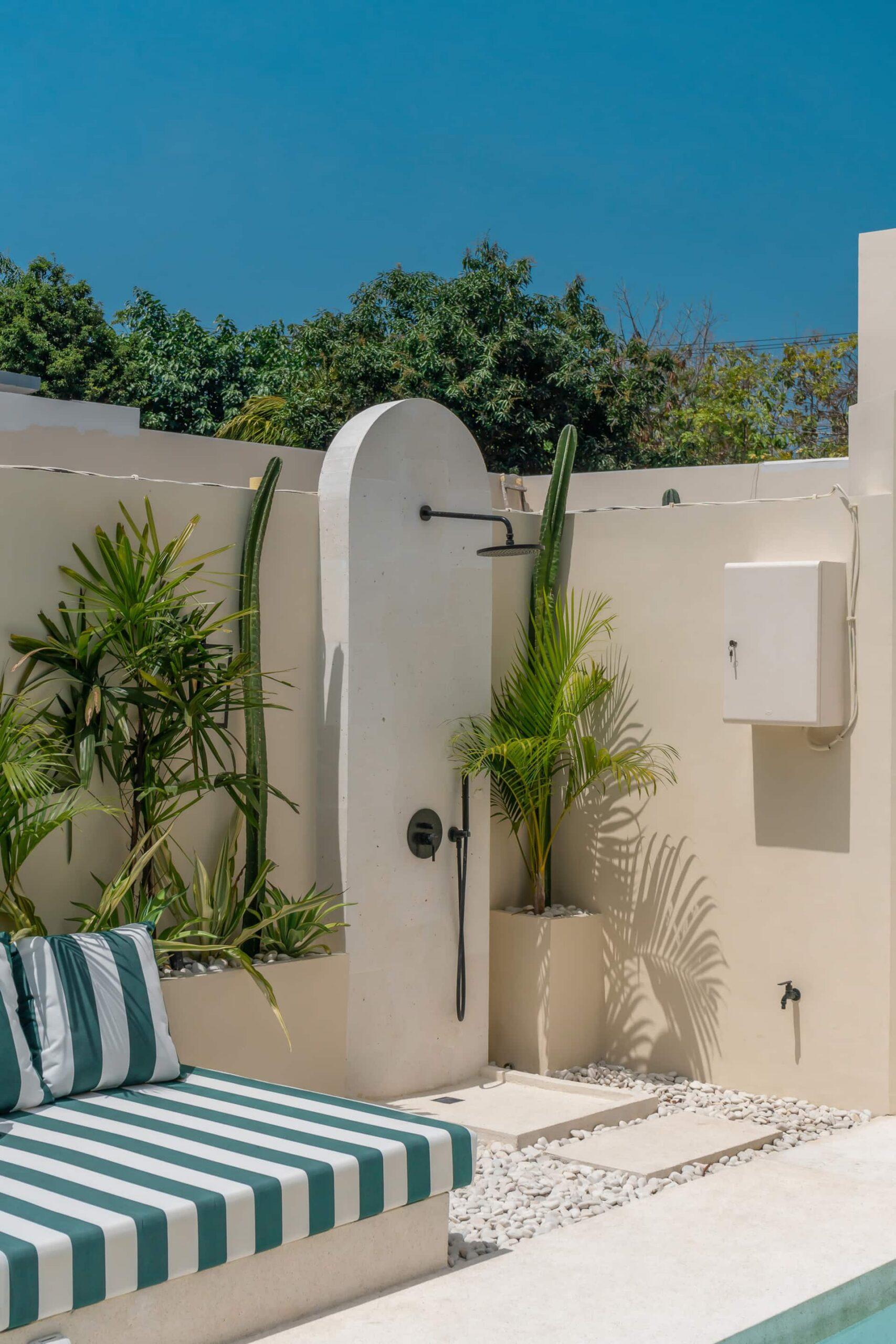 Outdoor rain shower set into a curved white wall beside the striped poolside banquette