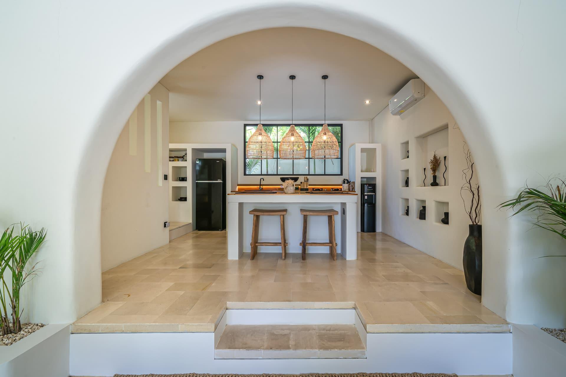 A wide plaster arch frames the raised kitchen, with an island, two timber stools and three rattan pendants