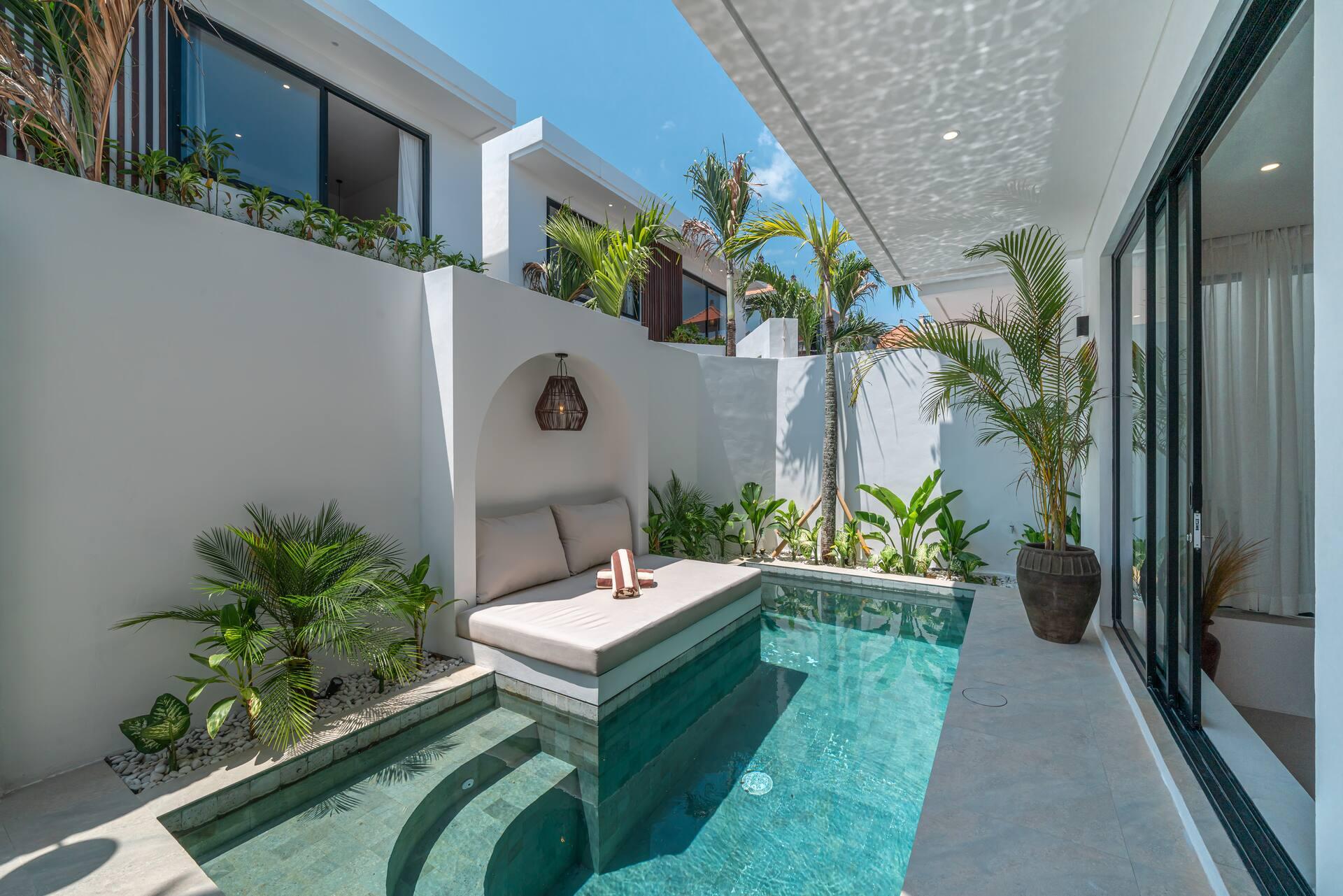 The poolside daybed at Villa Nyra, set on a plaster platform over deep green water beside the living room