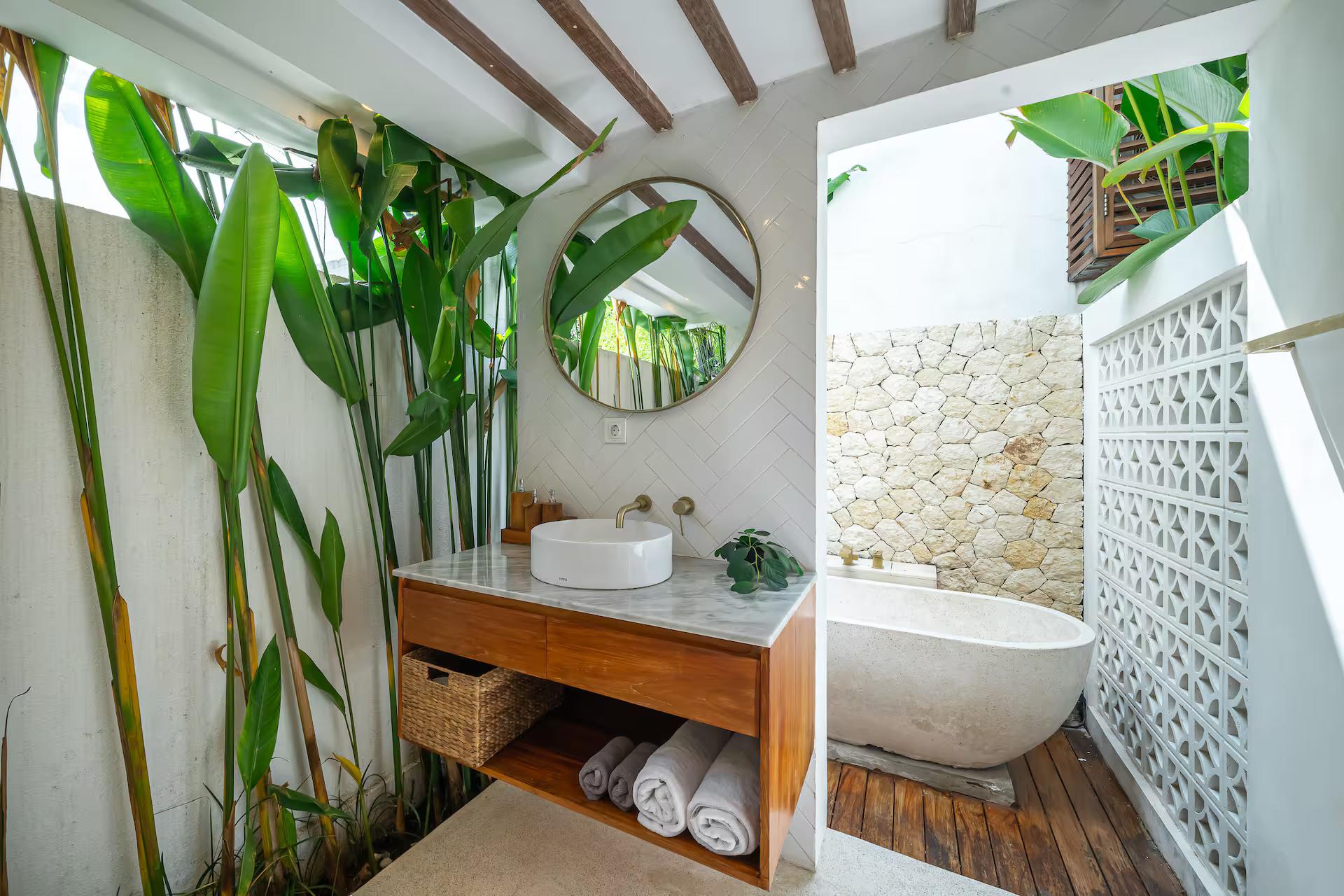 Open-air bathroom with a terrazzo tub, timber vanity and heliconia against coral stone