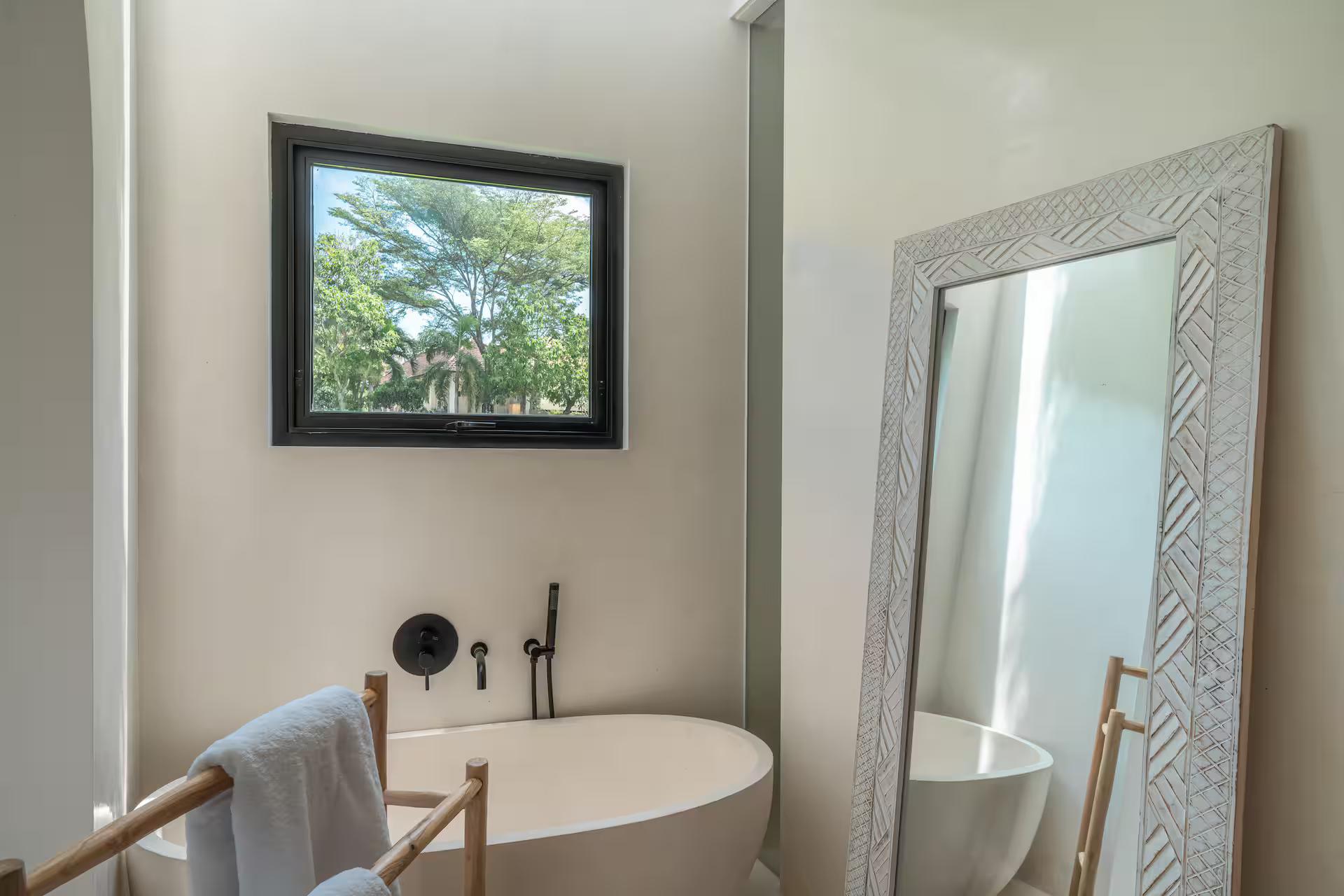 Freestanding oval bath beneath a carved white mirror, garden window alongside