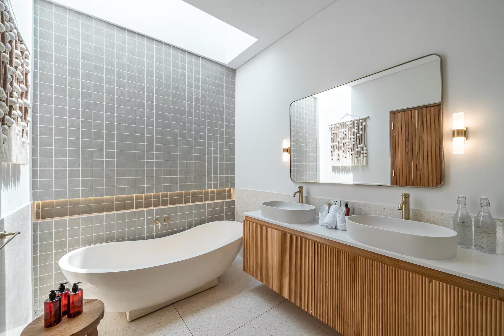 Freestanding oval tub under a skylight against a wall of sage-green tile in the en-suite