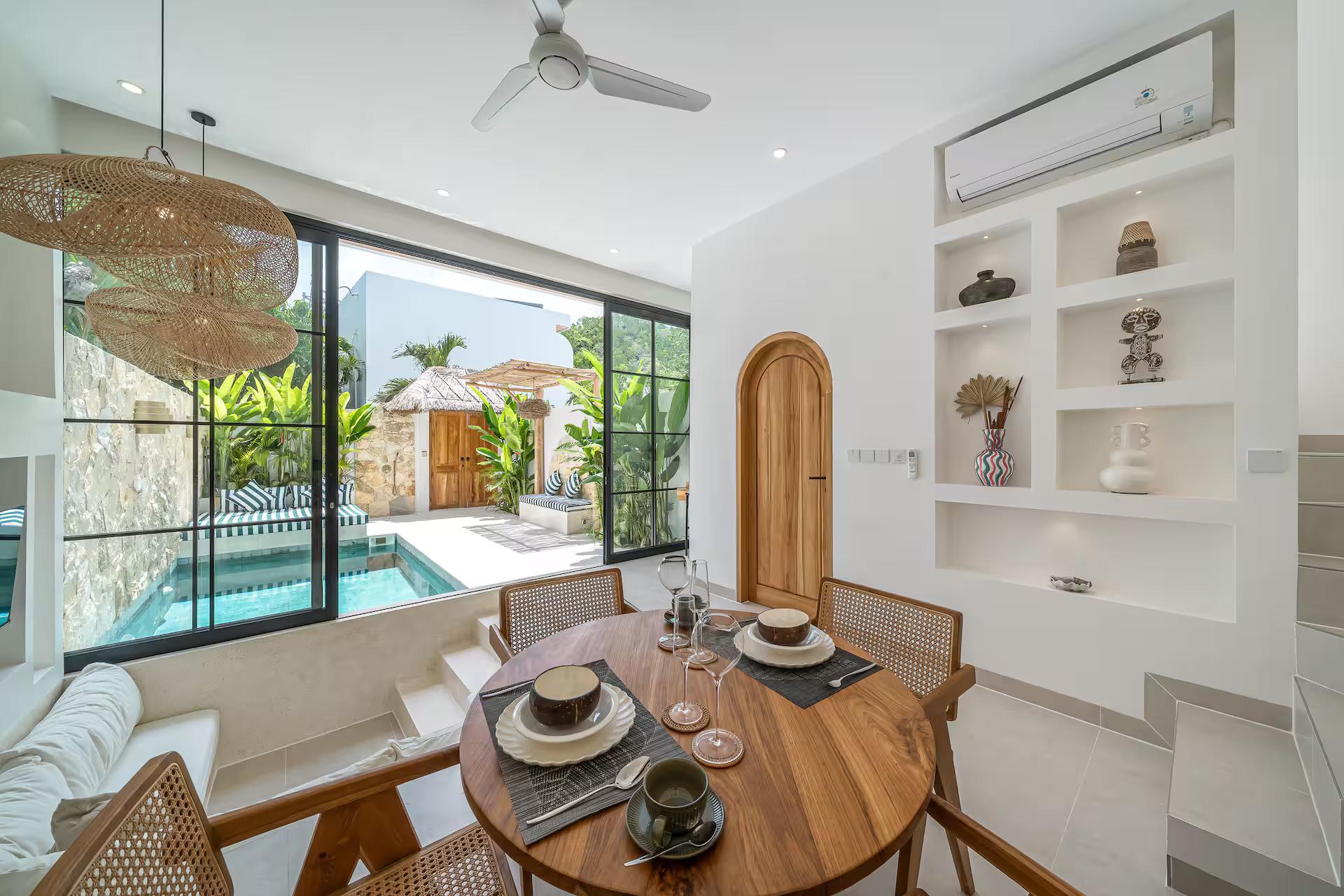 Round timber dining table with cane-backed chairs, the courtyard pool through the glass
