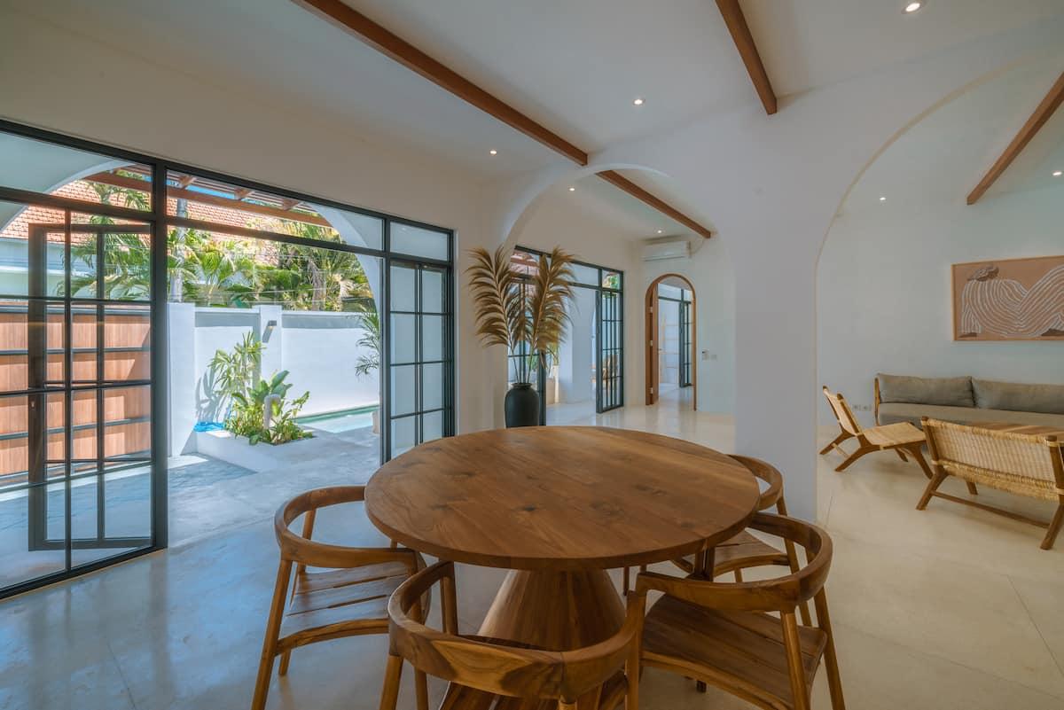 Round timber dining table and rattan chairs, steel doors opening to the pool courtyard