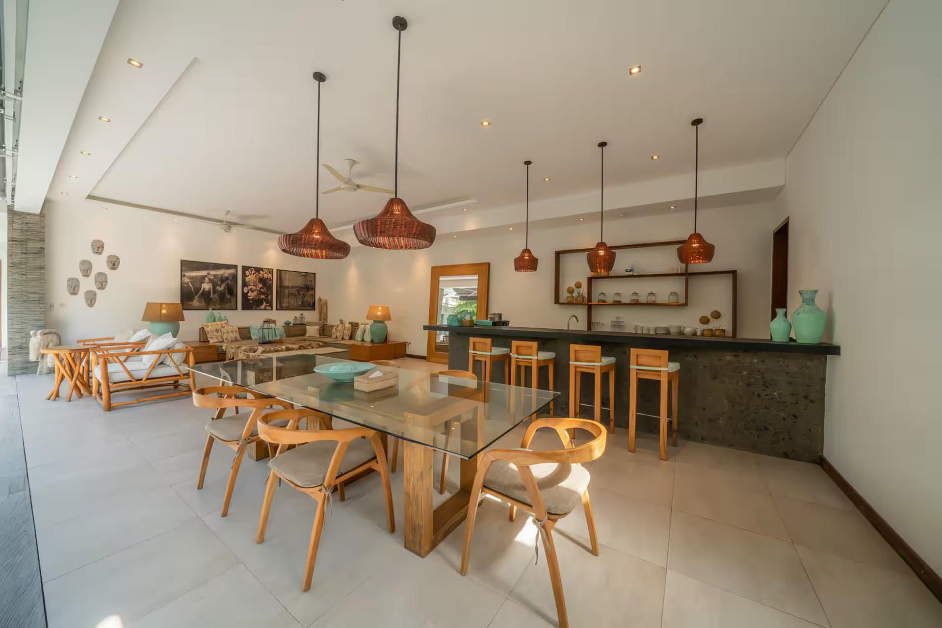 Glass dining table and stone bar counter beneath copper pendant lights