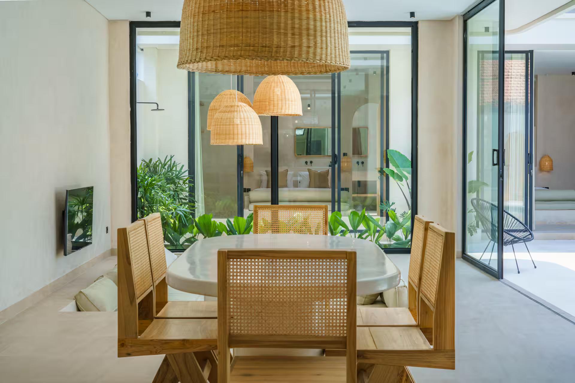 Round-ended microcement dining table with cane-backed chairs under woven rattan pendants