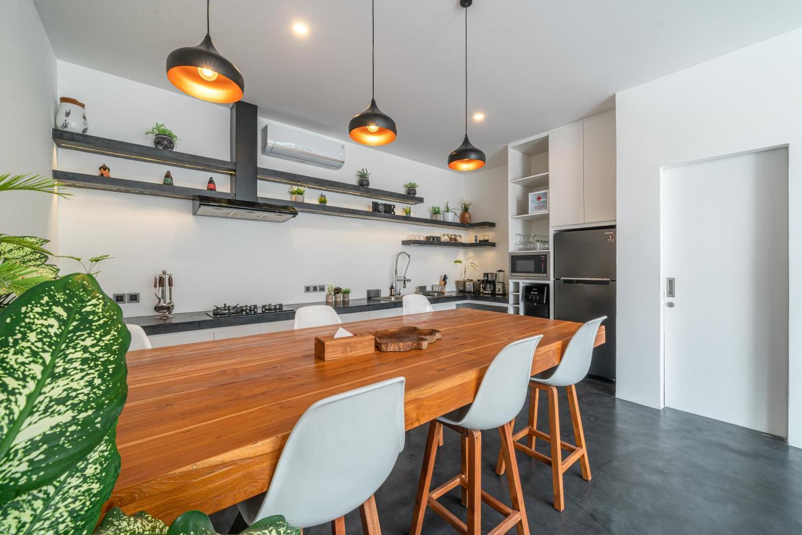 Long timber dining table with white chairs and orange-legged stools under dome pendants